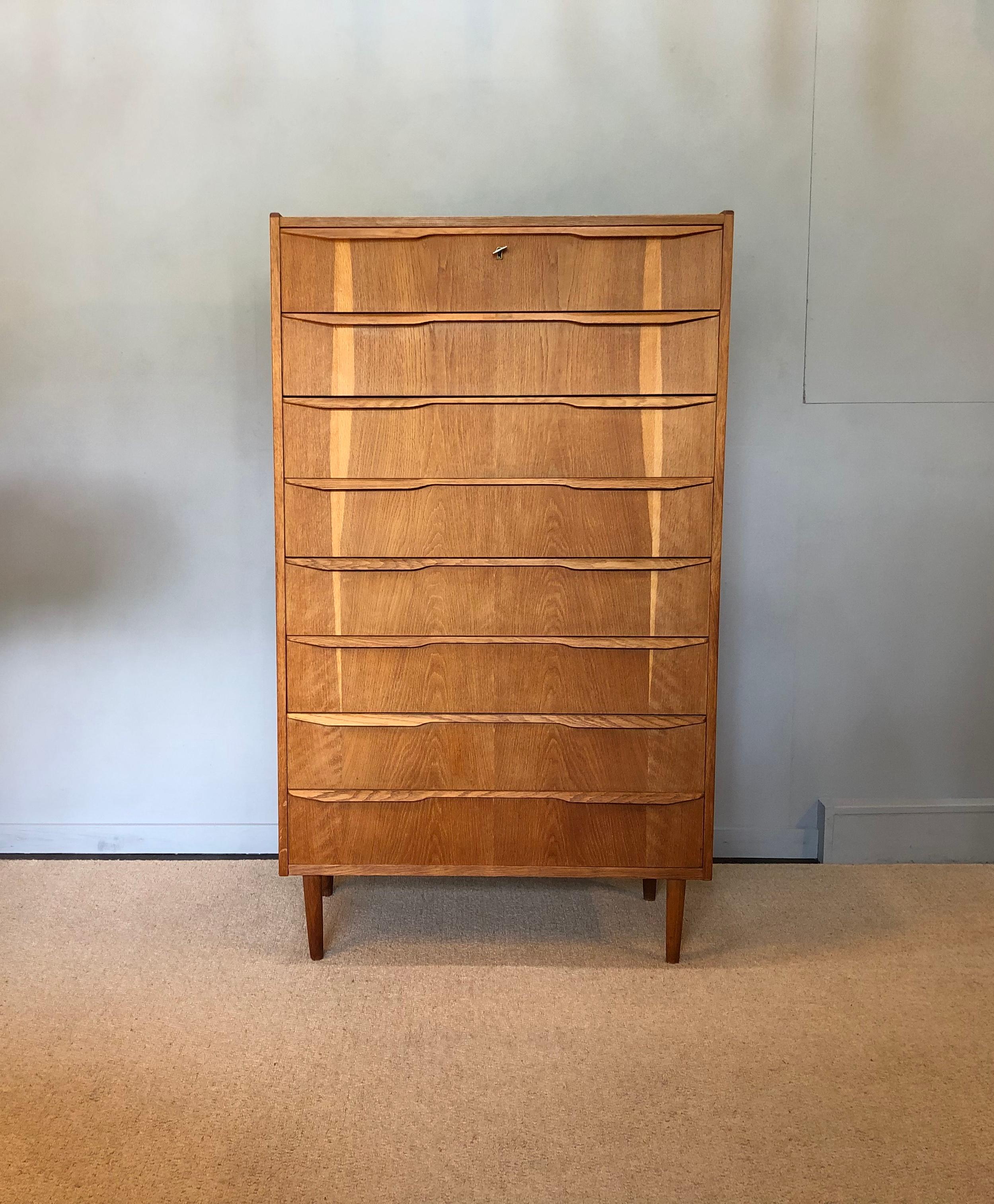 A superb large Danish midcentury oak tallboy. Produced in Denmark, circa 1960. Original key. Wonderful bookmatched oak front with sculpted lip handles. A great piece of Scandinavian modernist furniture.