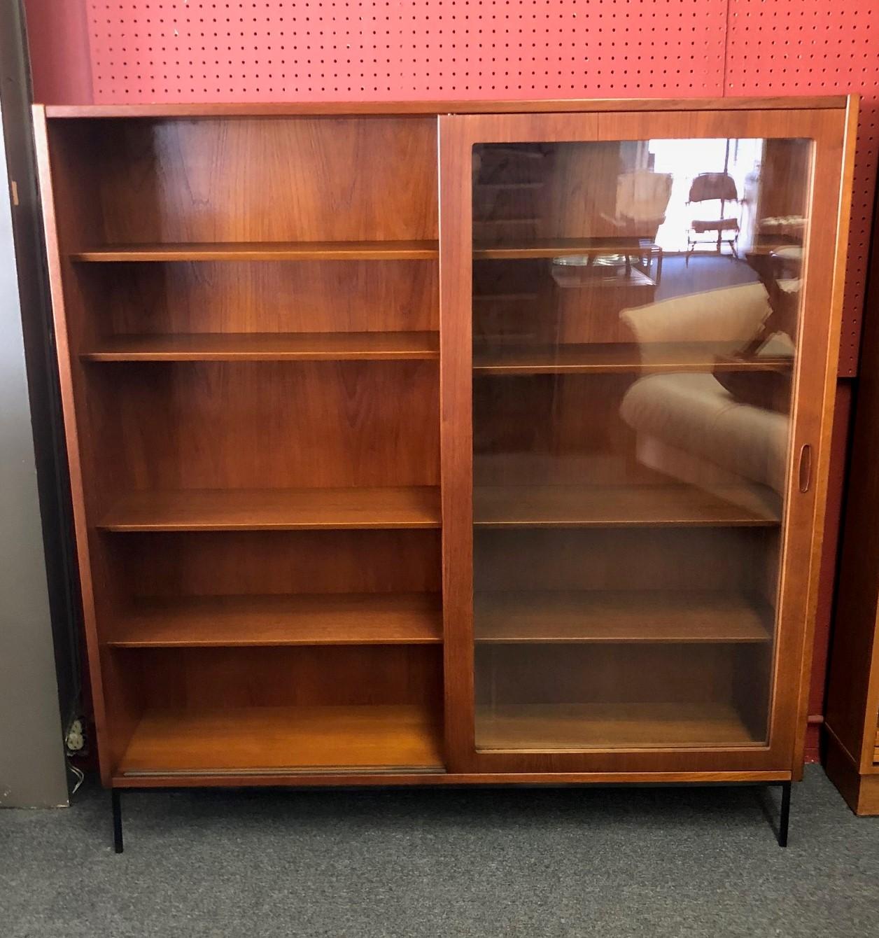 Large and versatile Danish modern teak bookcase, circa 1960s. The piece has adjustable beveled edge wood shelves with double sliding glass doors and sits on a solid iron base. It is a substantial high quality piece made in Denmark and measuring