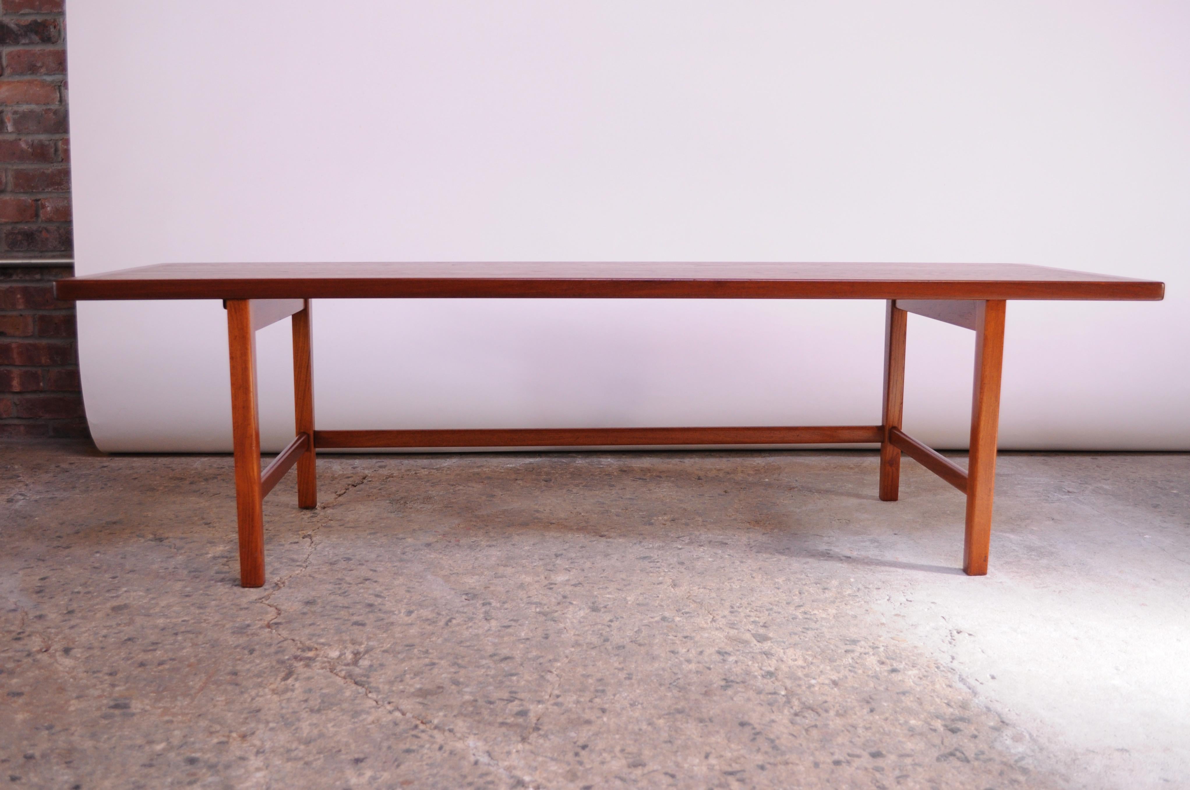 Dense Danish coffee table composed of a surface boasting vivid, rich teak veneer over solid wood with solid teak legs. Very well made and sturdy offering ample support to easily double as a bench. 
Conservatively restored condition; only minor wear