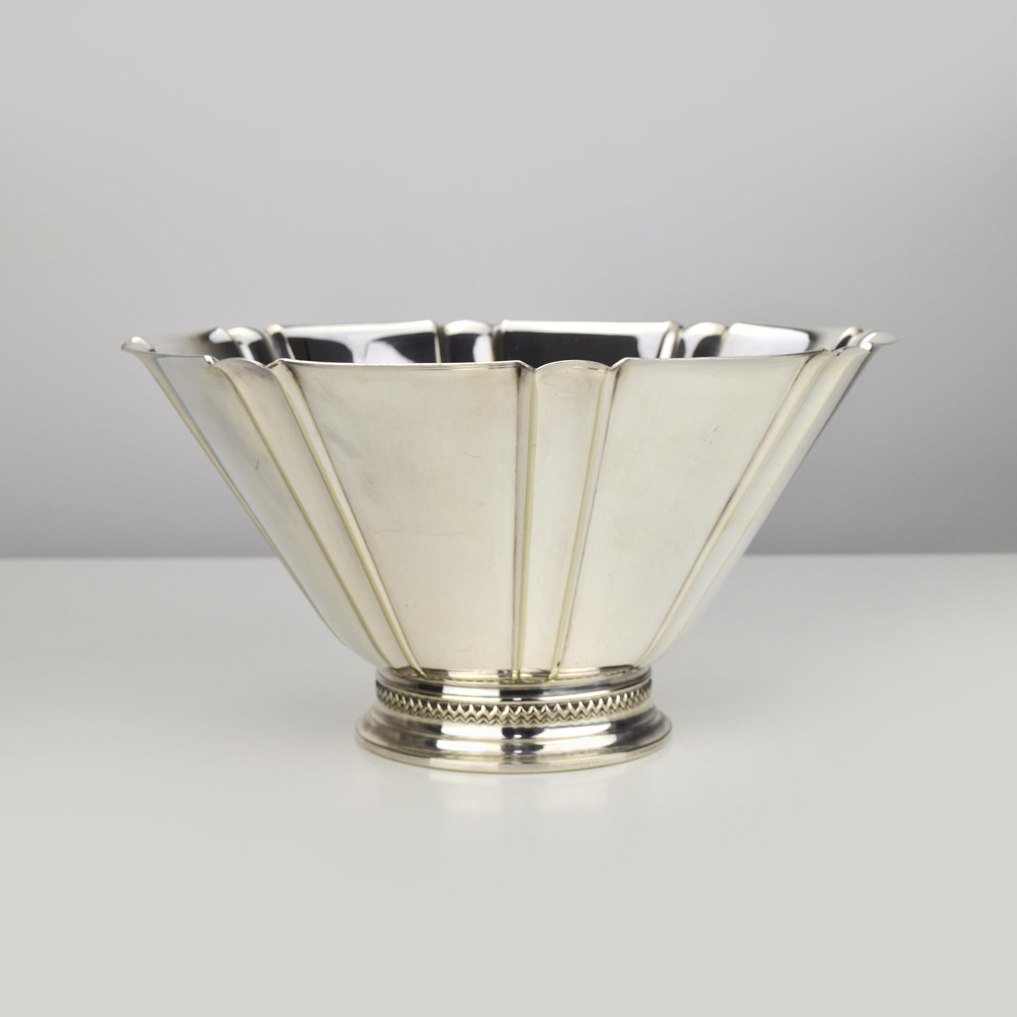 This elegant silver-plated bowl, crafted by Carl M. Cohr & Co. of Denmark, showcases a timeless Art Deco-inspired design. Featuring a scalloped, fluted body with crisp, clean lines, it is supported by a rounded base adorned with a delicate beaded
