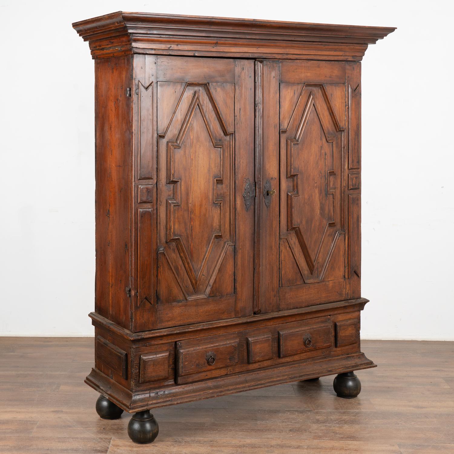 The heavy baroque style carving and paneling in the doors add to the visual impact of this handsome dark pine armoire.
The interior reveals three shelves, one large lower drawer all resting on bun feet.
This 6' tall armoire has been restored and