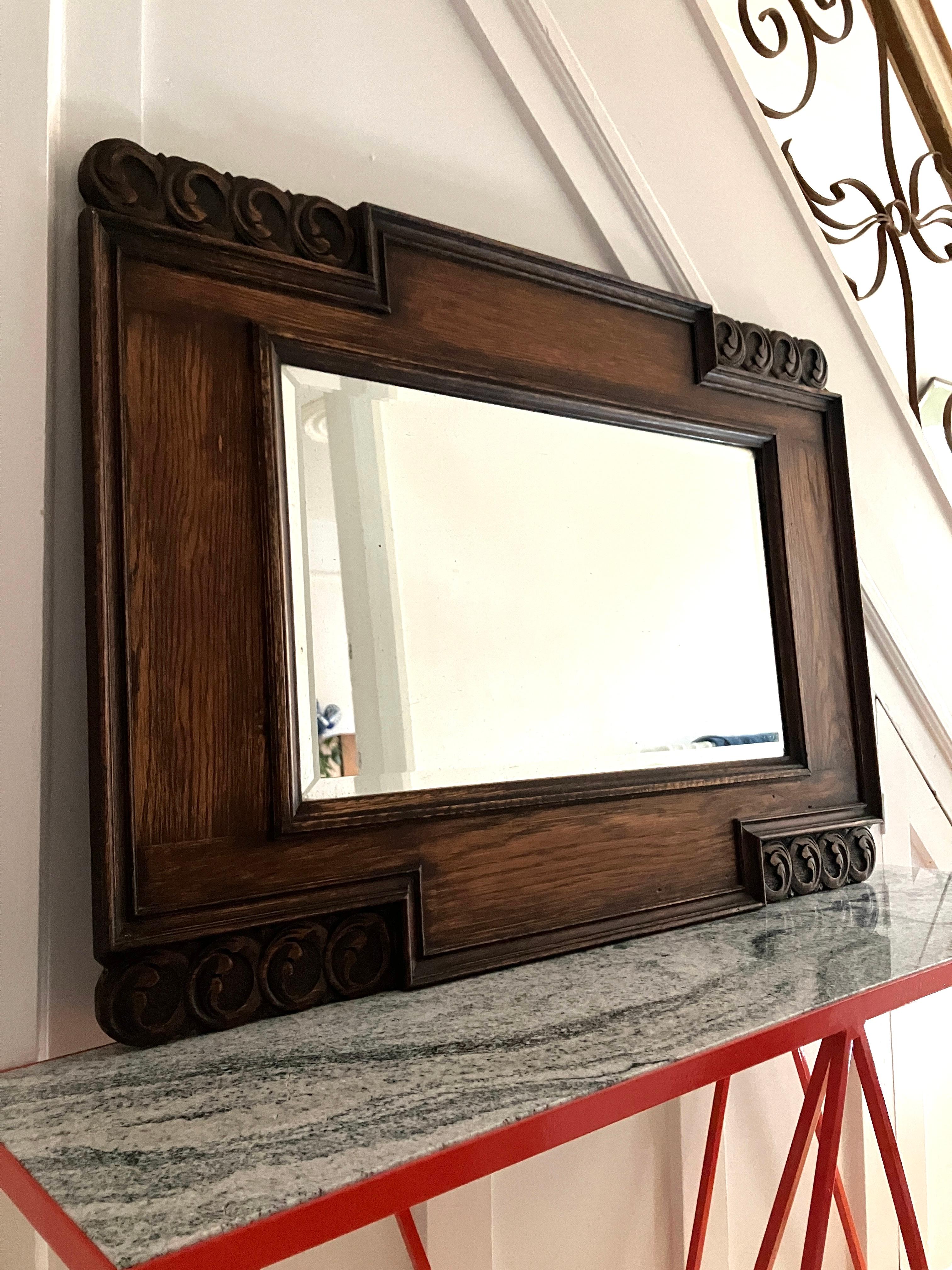 A handsome beveled mantel mirror with a thick oak frame. The frame is beautifully hand-carved with swirl decorations. 
Large size, ideal for above a fireplace. Size overall; 90cm wide, 66 cm high, and 3 cm thick. 
There is a wooden back and chains