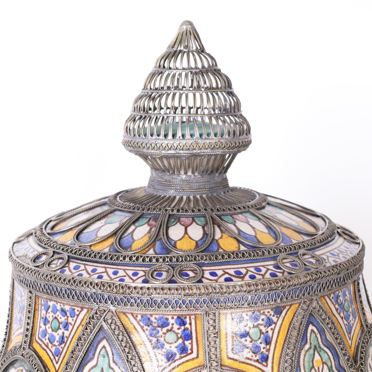 Large glazed terra cotta urn decorated with floral and geometric designs in traditional mediterranean colors and applied jewelry style metalwork taking this urn to the next level.