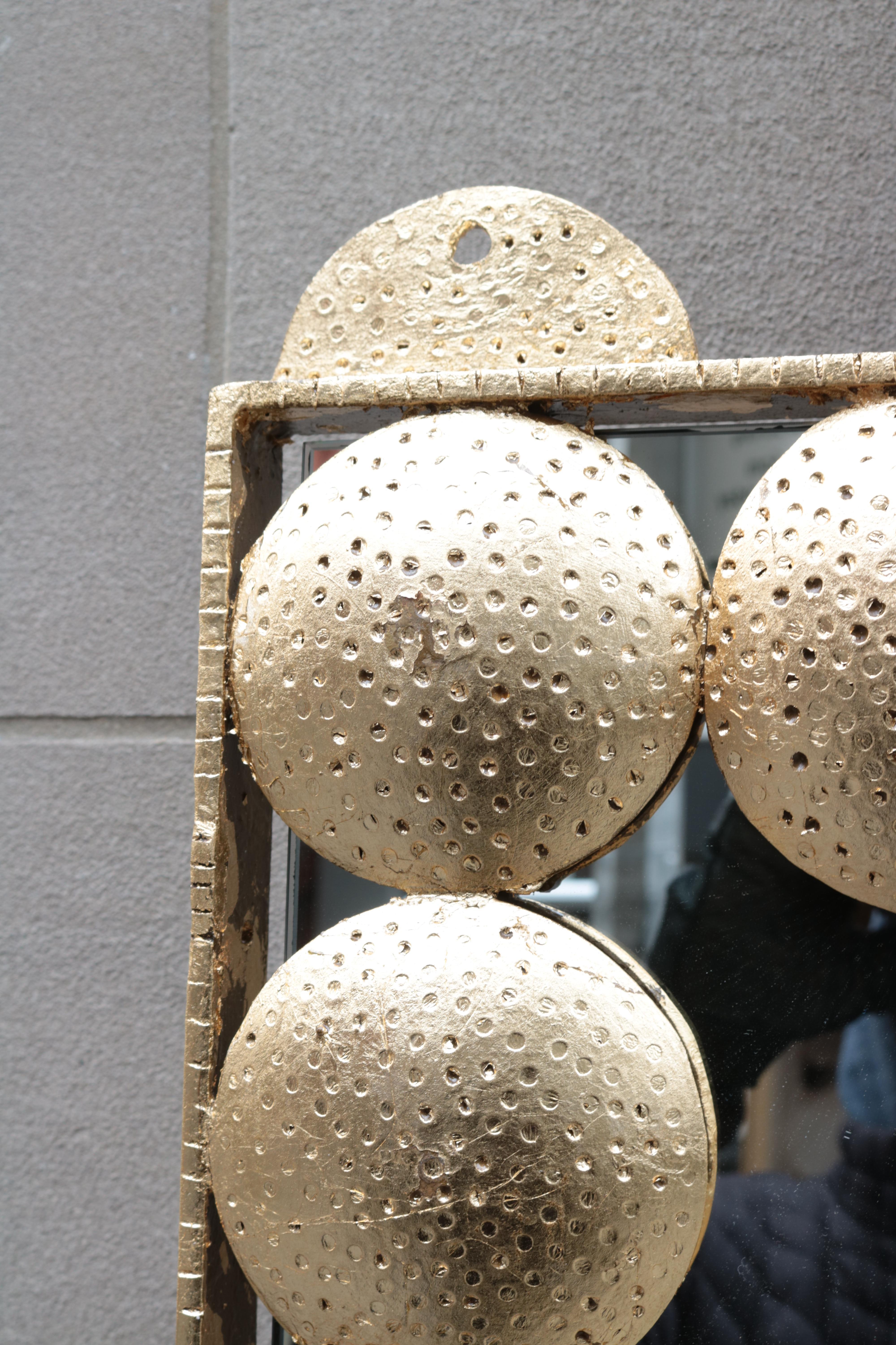 A large decorative brass wall mirror.
Central mirror surrounded by textured
brass circles and frame.

 