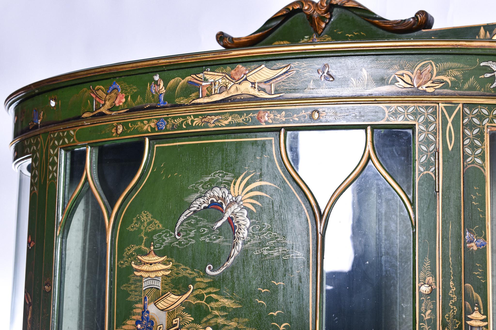 A Early 20th century large and very decorative, bow fronted green Chinoiserie lacquered cabinet. The centre panel displaying a fantastic Chinese scene, with arched gilded edges. Flanked by two glass panelled sections which also have raised, gilded
