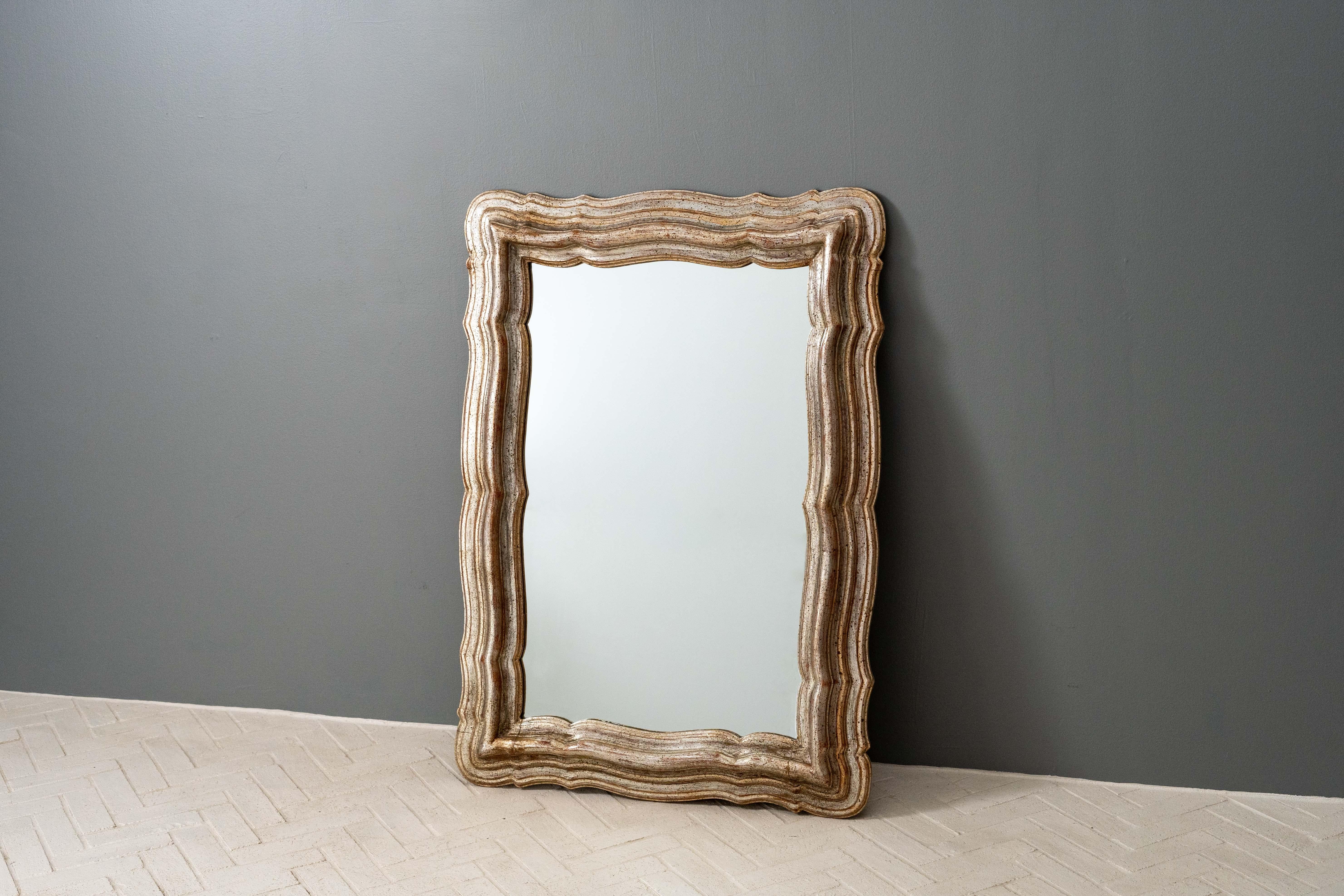 Italie, vers les années 1950. Un miroir mural fantastique, d'une grande ampleur et d'une grande présence. Variously and stepped / scalloped wood frame finished in silver leaf with various gold and silver washes. Dramatique et magnifiquement patinée,