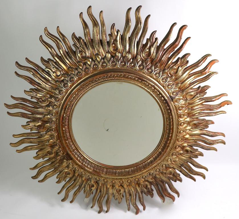 Large circular sunburst frame mirror with cast resin faux gilt frame. The frame has radiating rays surrounding the circular glass mirror. This item is in very good original condition, the center mirror has a minor dark spot, which is