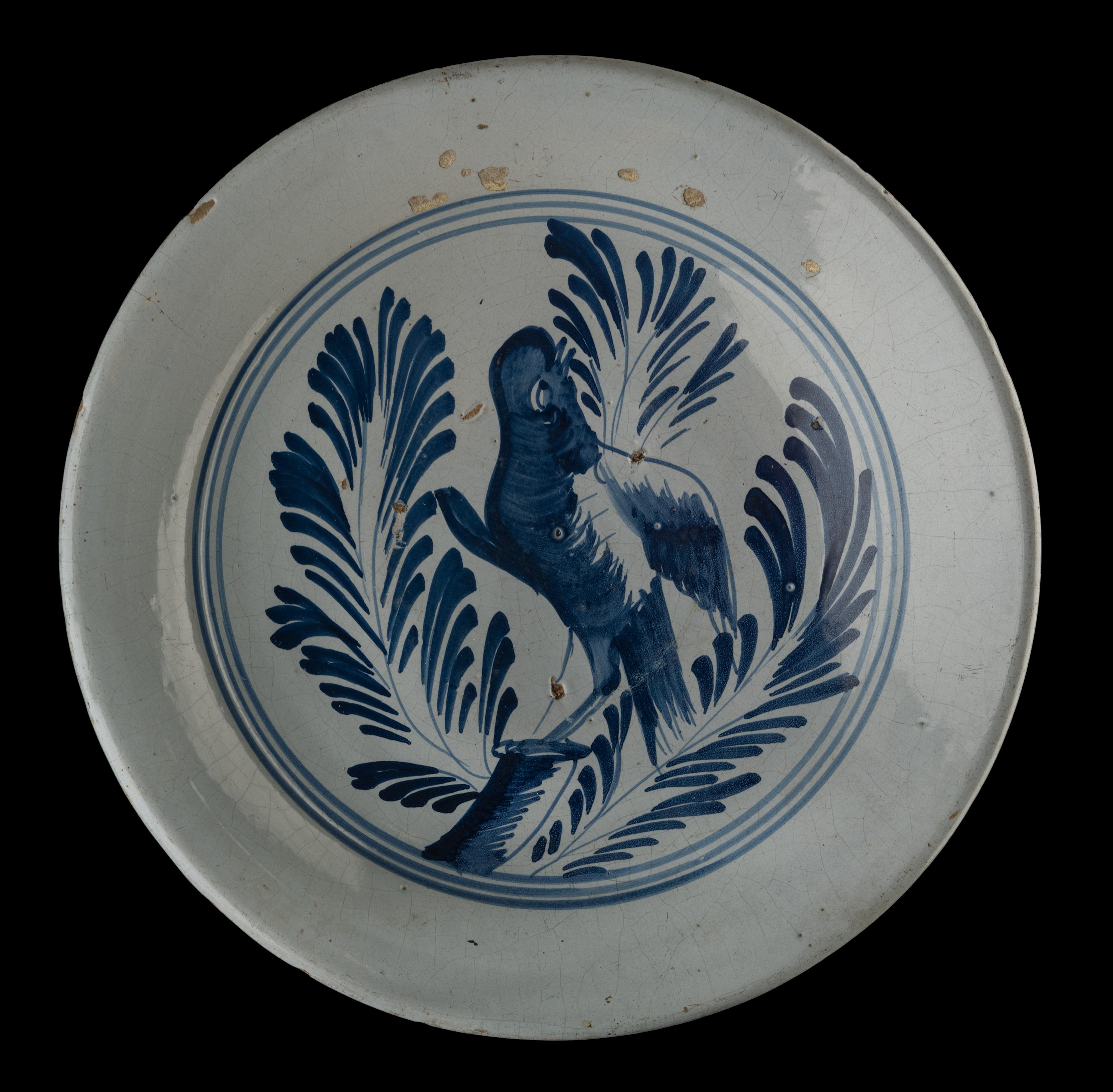 Blaues und weißes Ladegerät mit einem Vogel auf einem Ast. Harlingen, 1775-1800 
Raamstraat Töpferei. Maler: Pieter Ruurds 

Das Ladegerät hat einen leicht erhöhten Flansch und ist blau bemalt mit einem Papagei auf einem verkürzten Zweig, aus dem