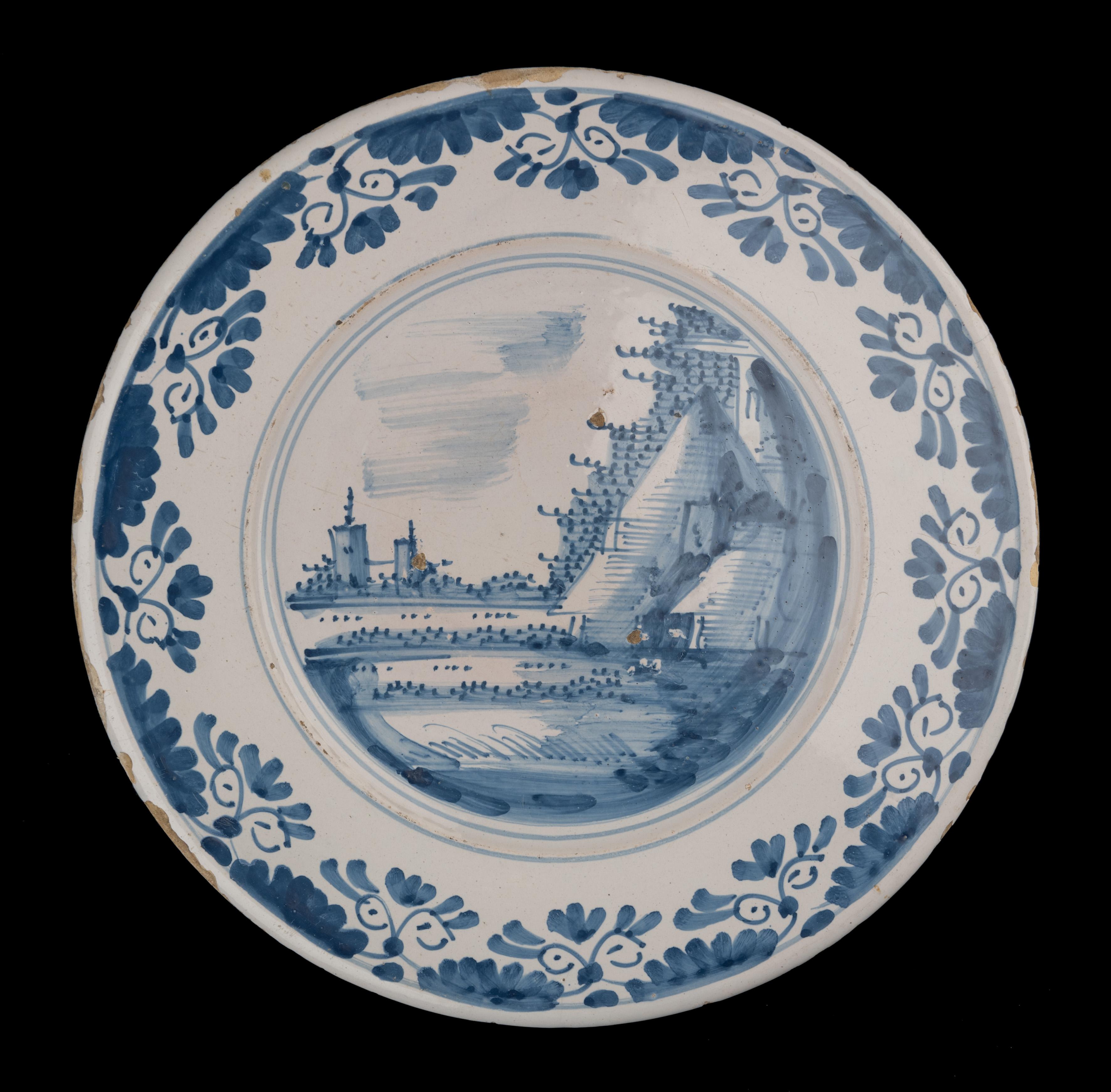 Large Blue and white charger with landscape
The Netherlands, circa 1660 

The charger has a wide, spreading flange and is painted in blue with a landscape in a double circle. The well is unpainted. The border is painted with striped segments and