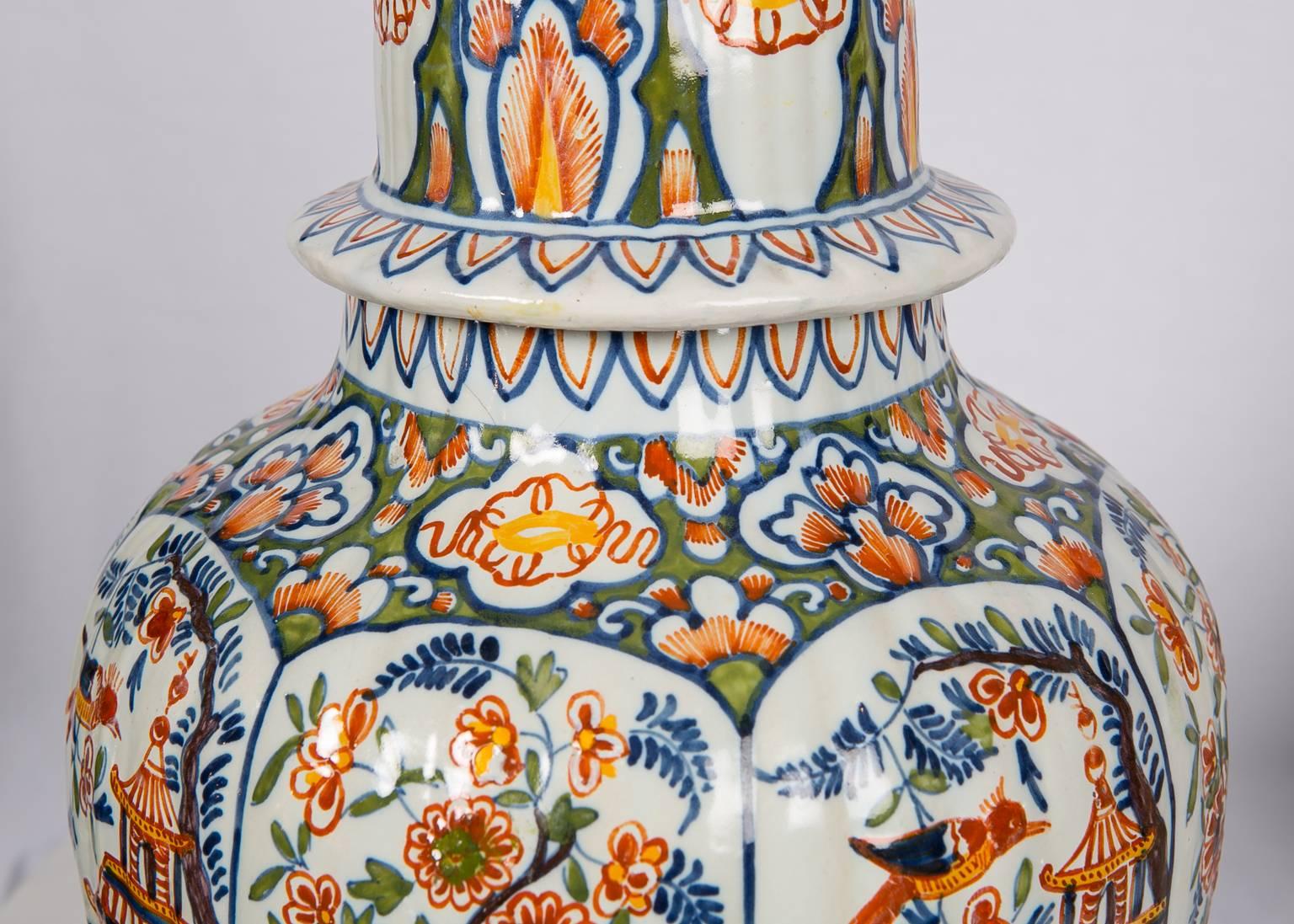 A pair of colorful Dutch Delft polychrome vases showing chinoiserie scenes painted in panels. In one panel we see a young woman with a basket of flowers standing before a pagoda, the other panel is filled with a  a flowering tree and a garden fence.