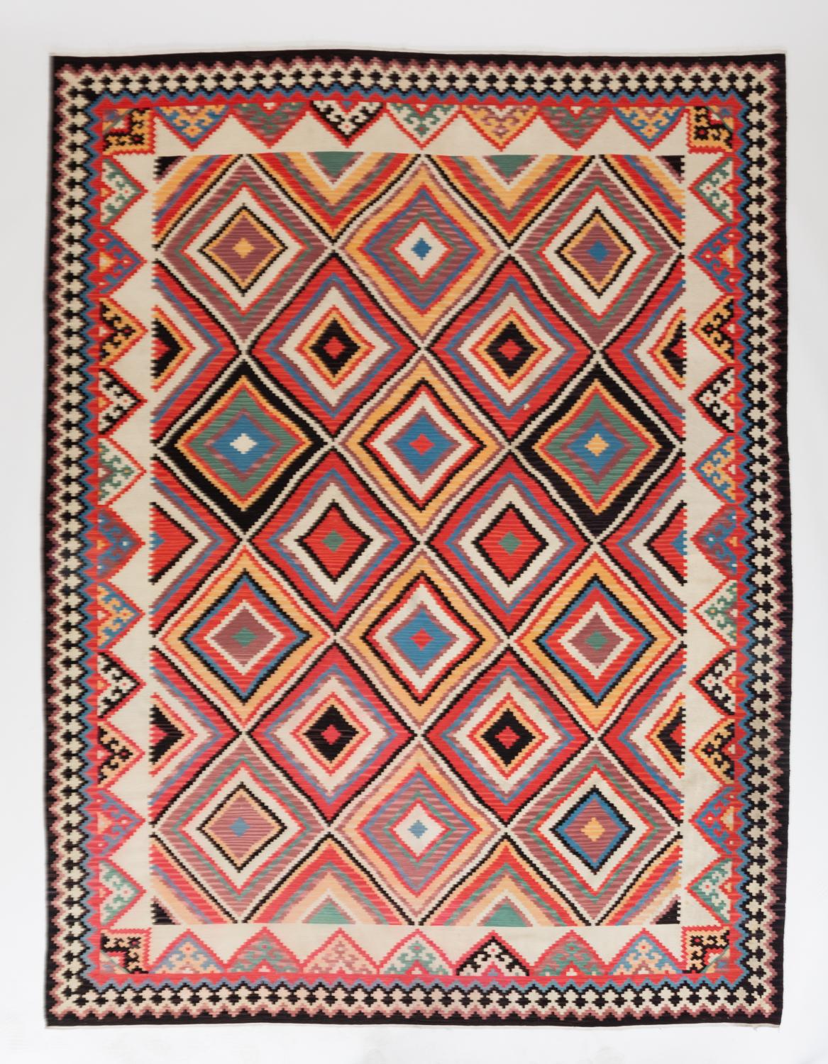 A traditionally woven Turkish Kilim area rug with a densely patterned design. The central field has a repeating diamond motif, surrounded by an off-white border and further dynamic geometry. Woven in wool and cotton fibers with a bright color scheme