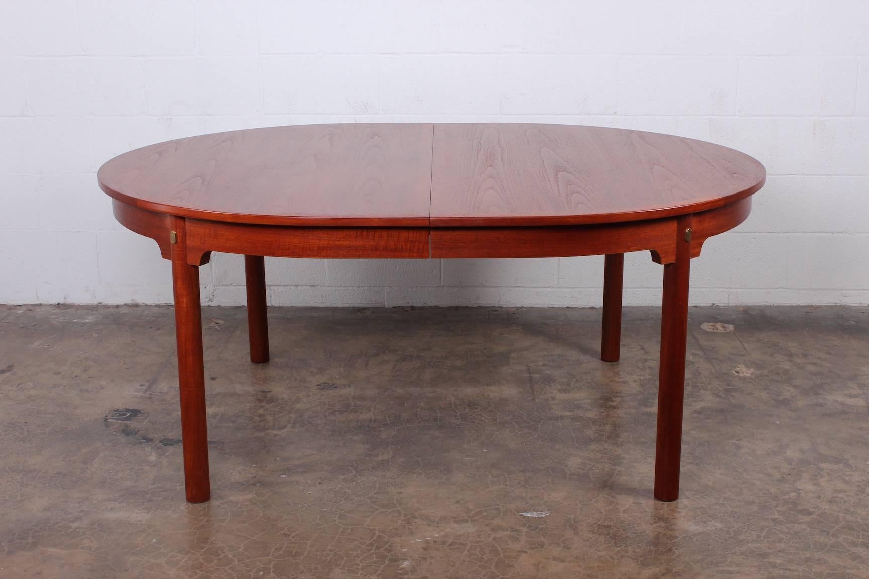 A large teak dining table with brass details. The table measures 66.75