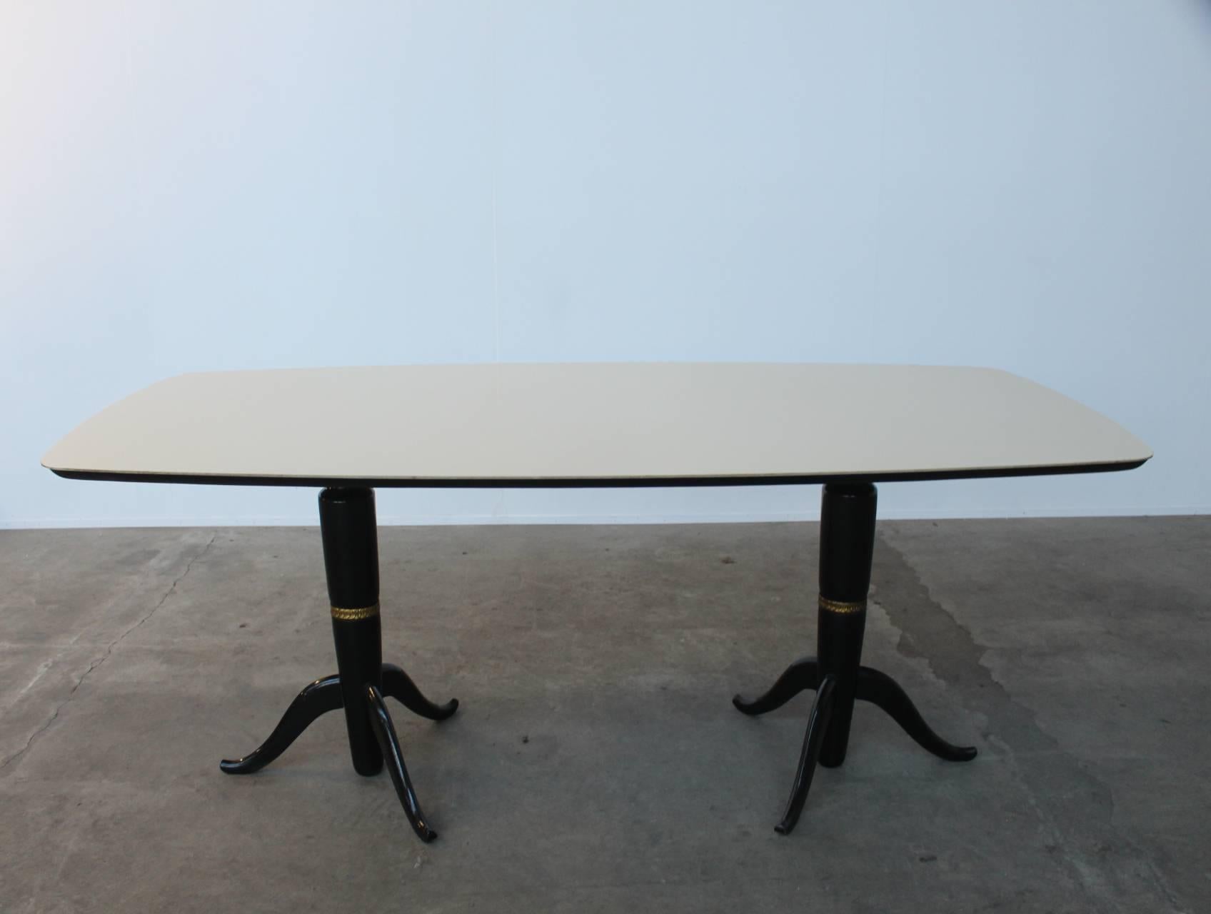 Large dining table in the style of Osvaldo Borsani. The top rests on two ebonized three-legged pedestals with beautiful giltwood details. On top of the desk lies a wonderfully milky white coloured Murano glass top. There's one little chip to the