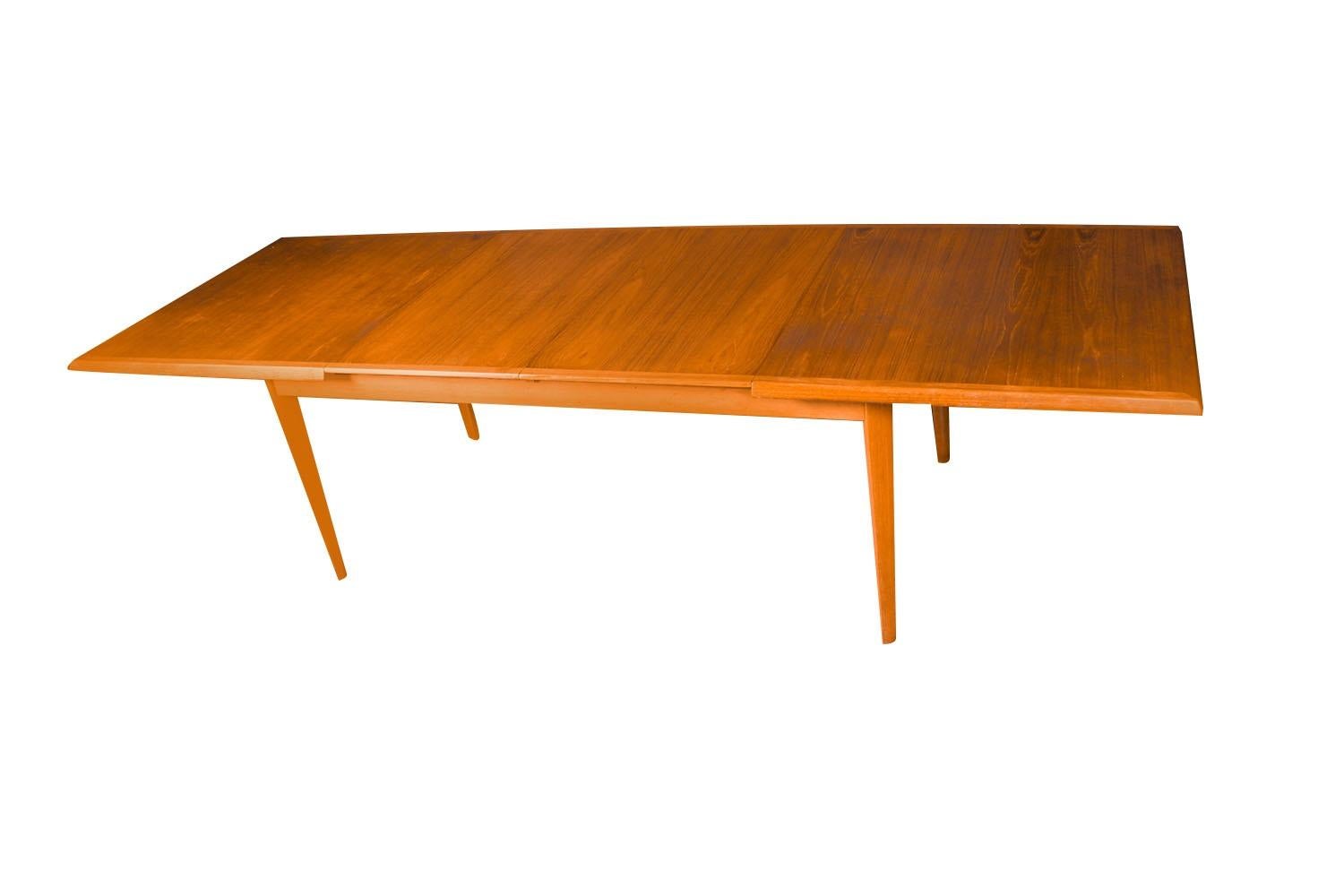 Beautiful large Danish, teak Mid-Century Modern expandable dining table. Features richly grained, teak top. Raised over four tapered legs, creating a clean and elegant profile. This remarkably large dining table comes with two extension leaves to