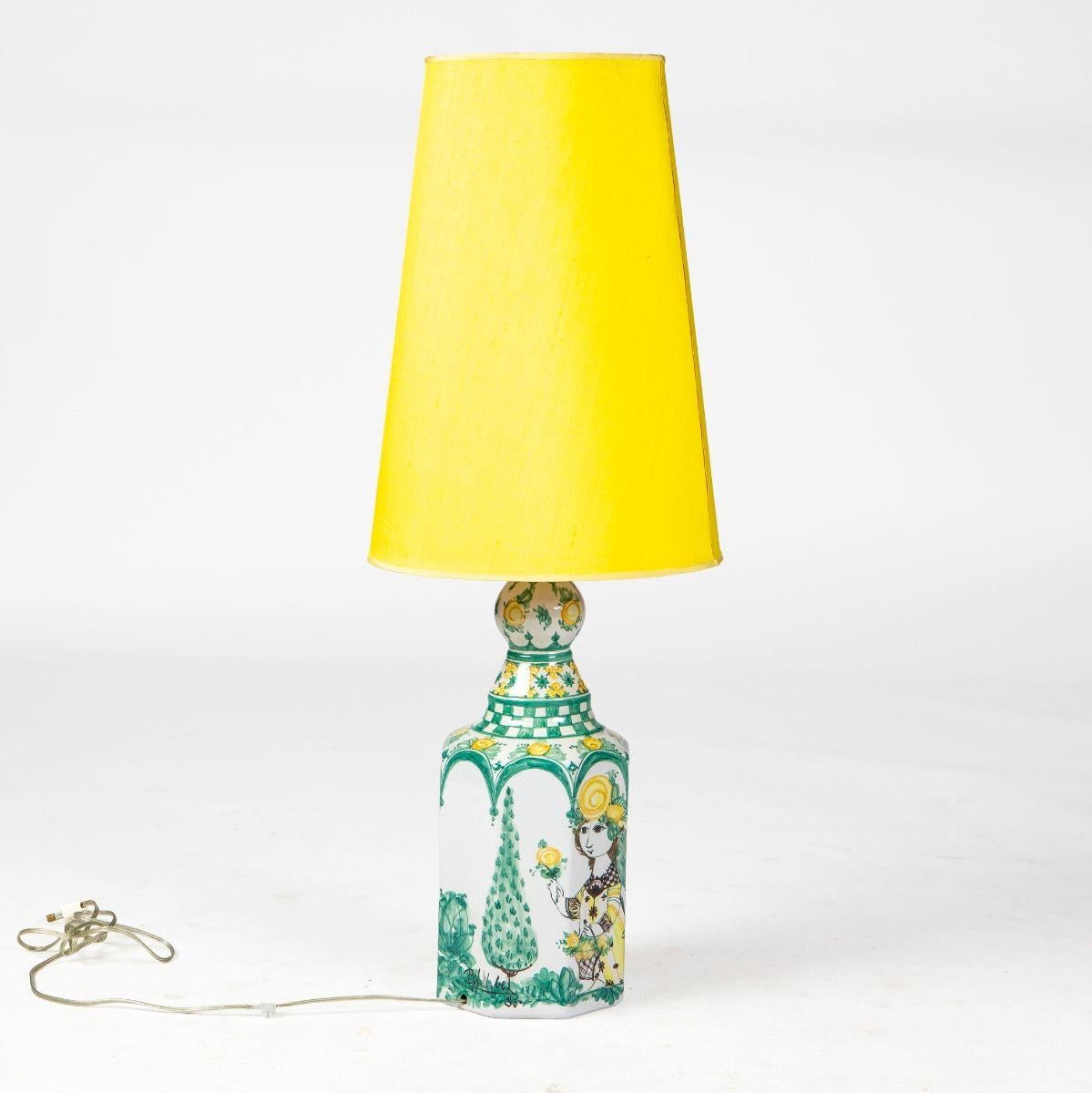 Large, distinctive table lamp in glazed ceramic by Bjørn Wiinblad (1918–2006).
The lamp is octagonal in shape and richly decorated with polychrome glazes in green and yellow tones. The motif depicts a woman surrounded by yellow roses and green
