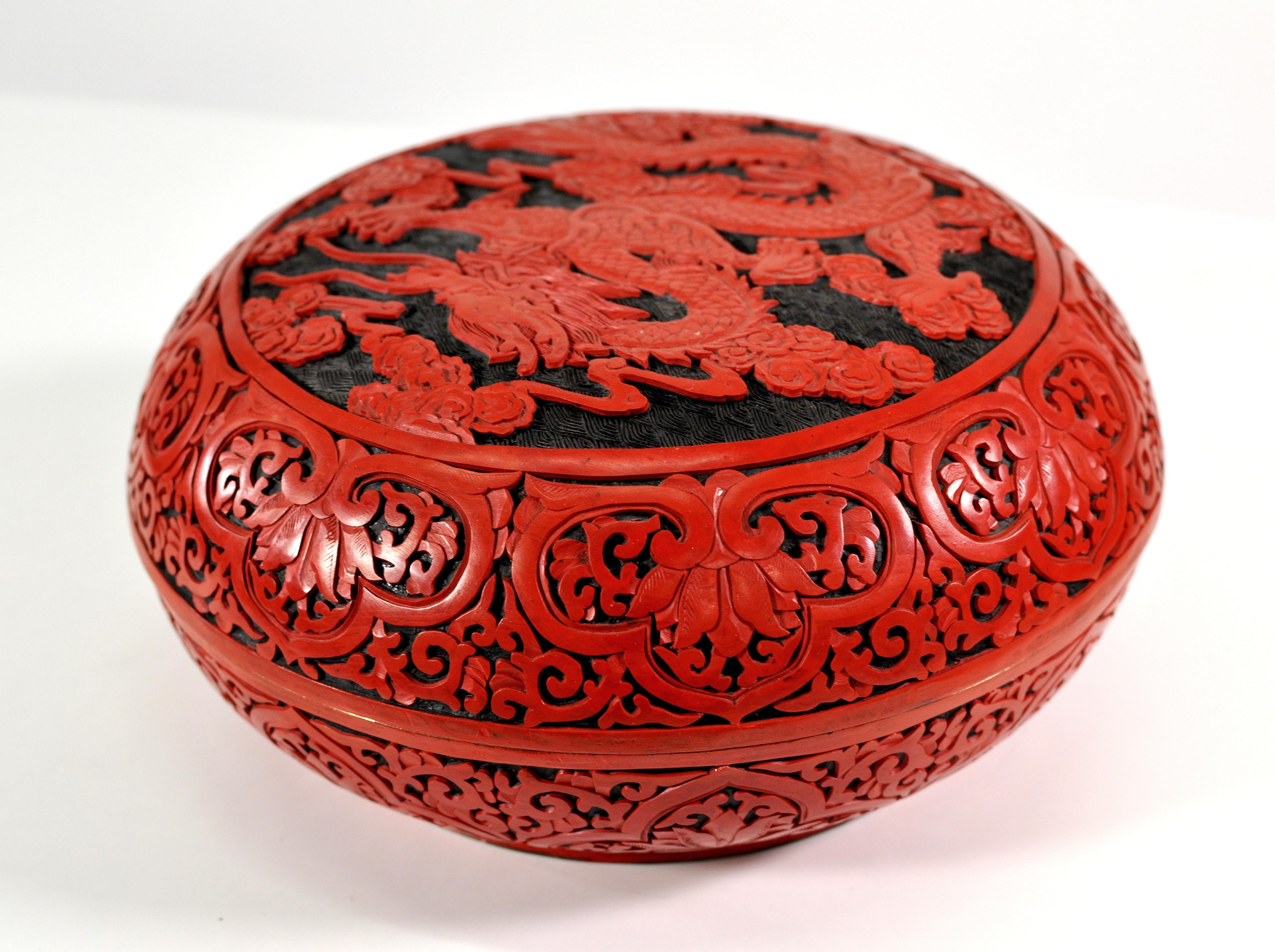 A large vintage Chinese red cinnabar box with deep relief carved lid depicting flowers, leaves and a dragon. The round box has a domed lid and a black lacquer interior.