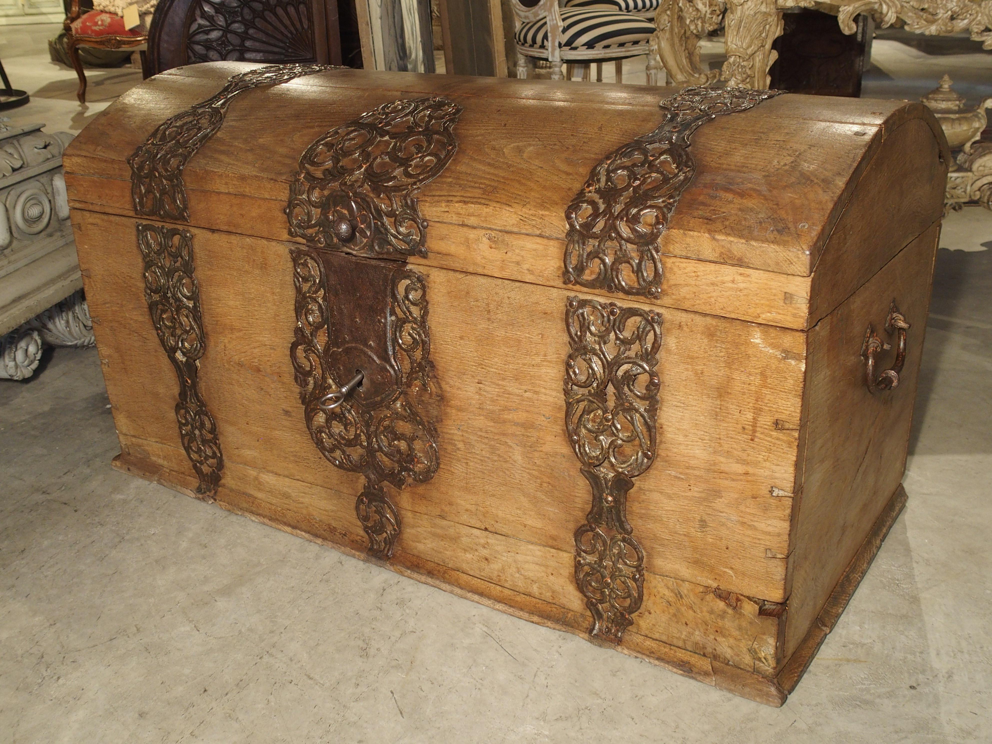 This large, natural colored oak trunk from Germany is from the beginning of the 18th century and features magnificent and wide, pierced, scrolling, iron strapping. The motifs, which cover a substantial portion of the façade as well as the domed top,