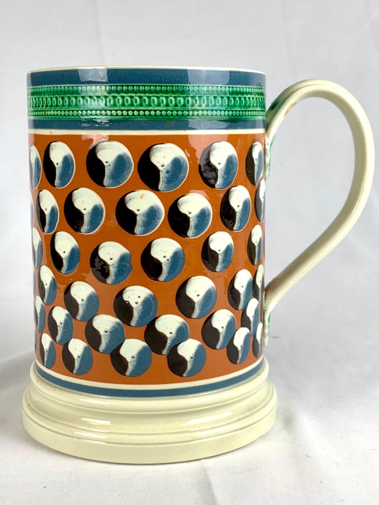 Esta taza grande de mochaware fue fabricada por Don Carpentier, un alfarero conocido por sus recreaciones de la cerámica americana e inglesa de principios del siglo XIX decorada con engobe utilizando un torno accionado con el pie.
El diseño presenta