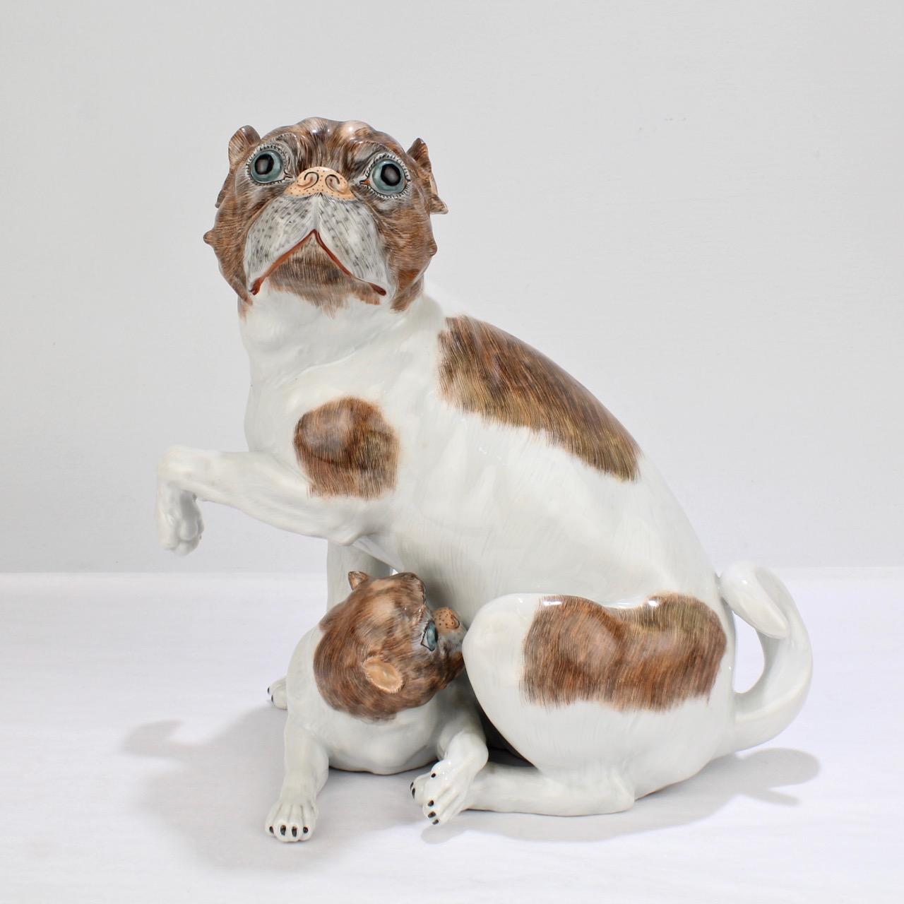 A wonderful Dresden porcelain figurine of a mother pug and her puppy.

The figurine is modeled after the 18th century Meissen figurine by Johannes Kaendler with the puppy nestled snugly under the mother's belly. 

Each dog is decorated in brown