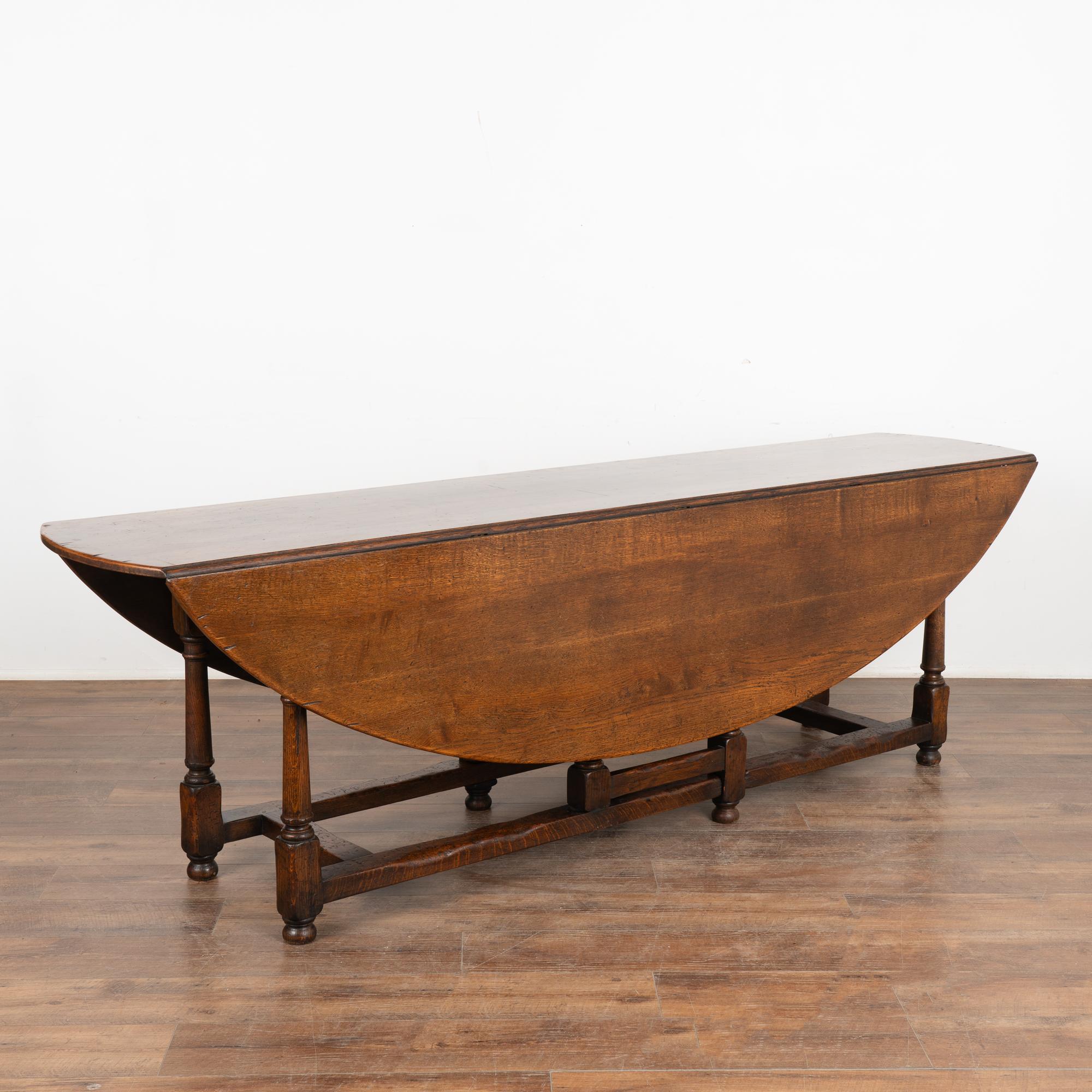 This handsome gateleg dining table is also known as an English wake table with drop leaves.
Notice the dark patina of the oak, aged and naturally distressed over generations of use and lovely turned legs.
The large oval shaped top has 2 drop leaves,