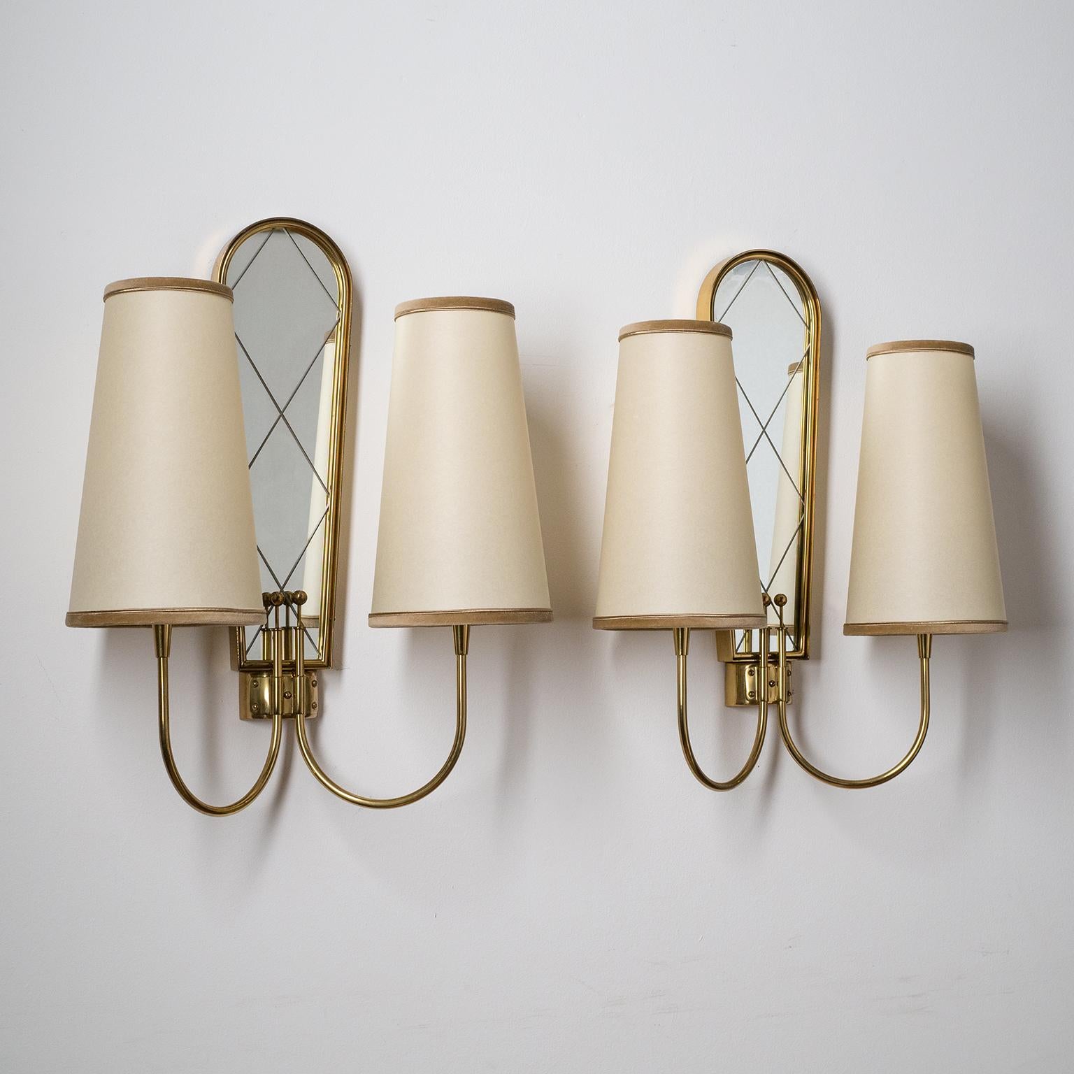 Rare pair of large dual-arm brass wall lights from the 1940s. Brass hardware with a mirror centerpiece. Each arm has a frosted glass disc which sits under the socket and on to which the shades are placed. Good original condition with some patina on