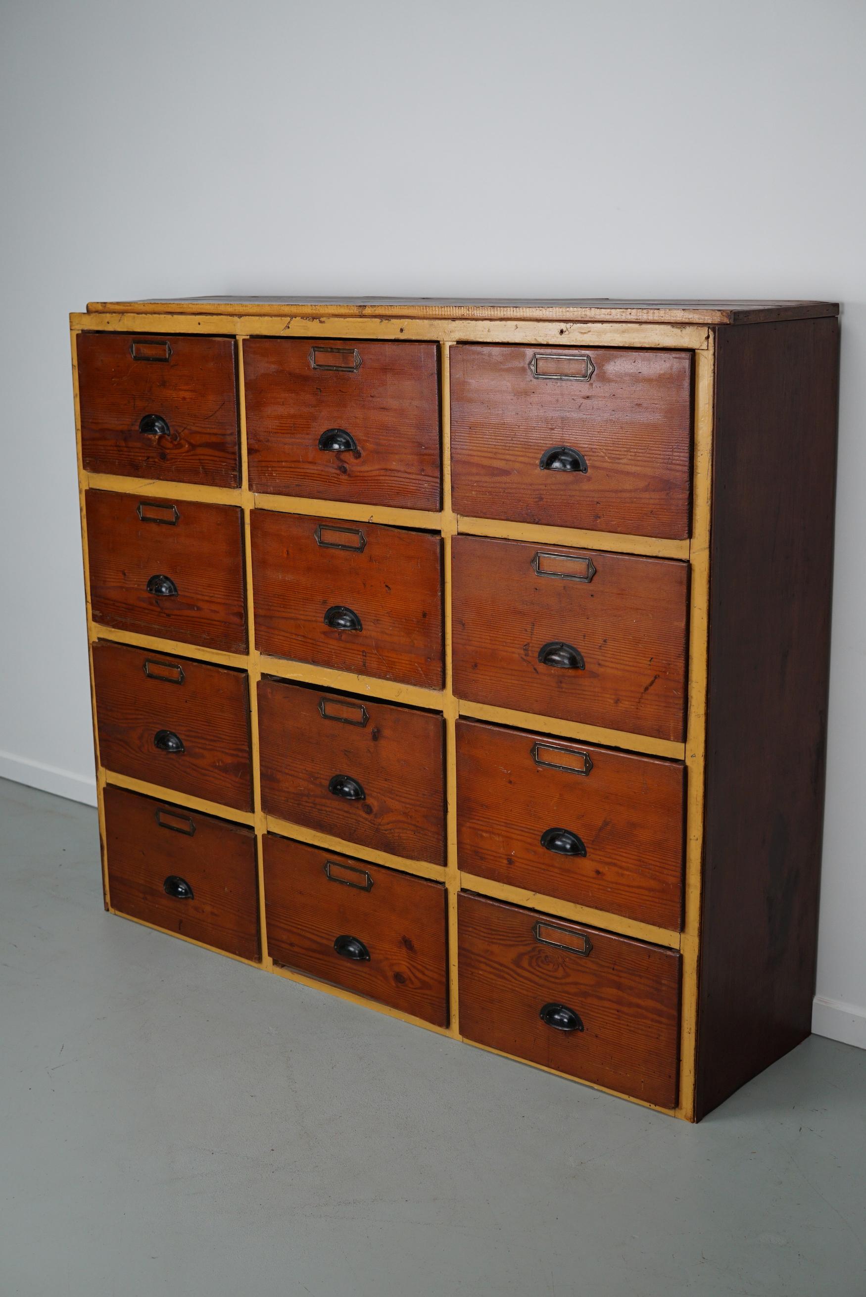 This workshop cabinet was made from pine in the Netherlands circa 1930s and it was used in a workshop for dentist equipment. It features 12 very large drawers with black handles. The interior dimensions of the drawers are: DWH 35 x 41 x 26 cm. The