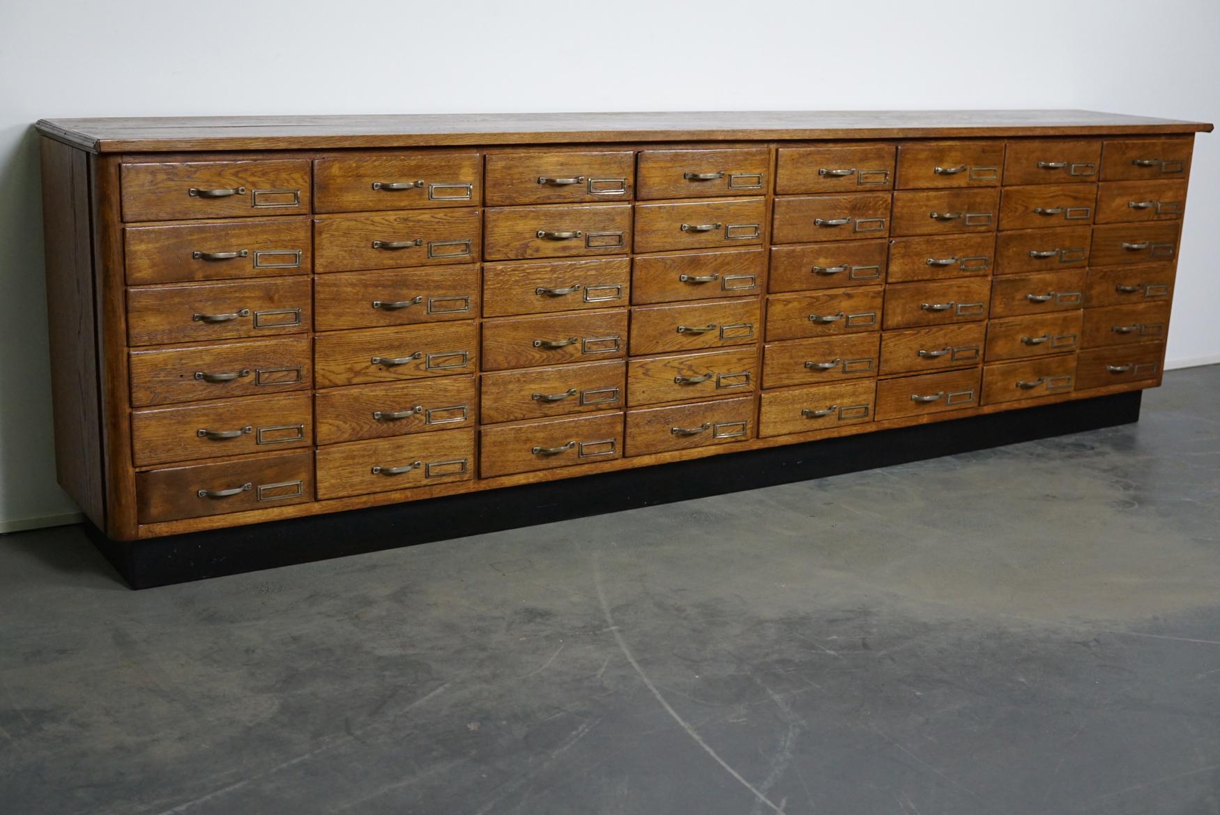 This large oak apothecary cabinet was made circa 1940s in the Netherlands. It features 48 drawers with metal handles and name card holders. It was originally used in a shop for lightning supplies in the city of 's-Hertogenbosch. Some of the drawers