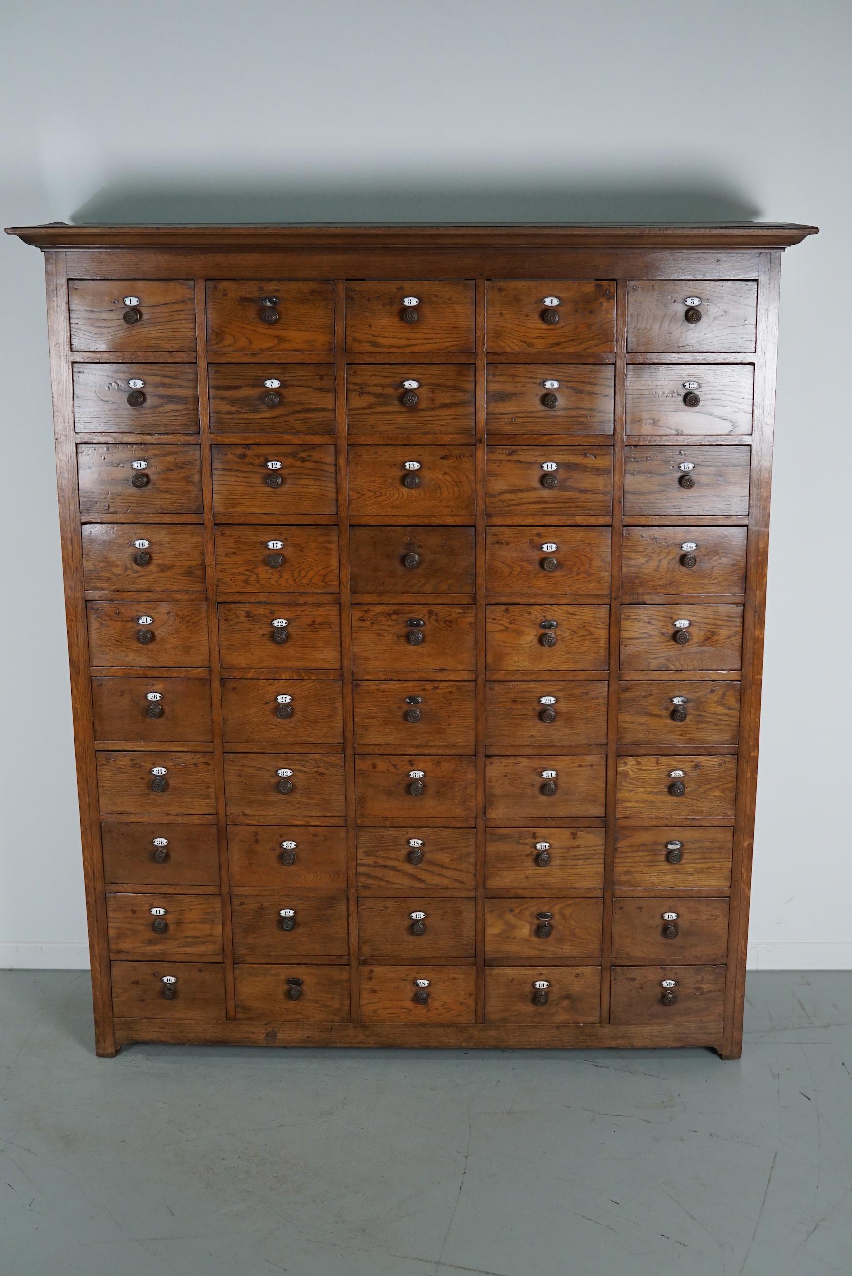 This apothecary cabinet was made circa 1900s in the Netherlands. It features 50 drawers with amazing brass knobs and enamel number shields. It was originally made for a barber and it was used to store the individual shaving supplies of the