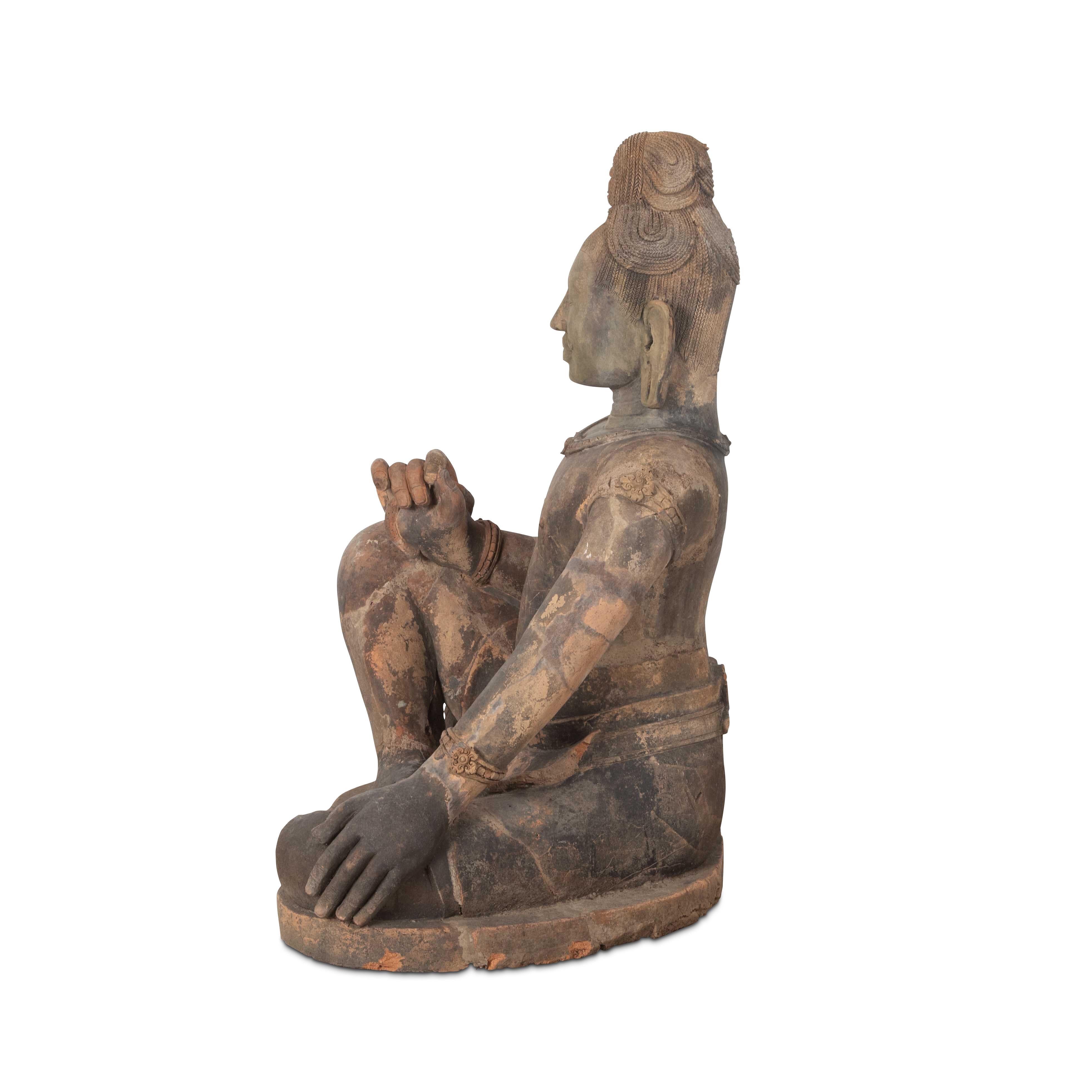 A very rare larger than life size late C18th/early C19th terracotta figure of a male diety, in the Khmer style, the figure sitting in a relaxed pose, with hair tied up and a serene content expression on his face. Featuring beaded bands around his