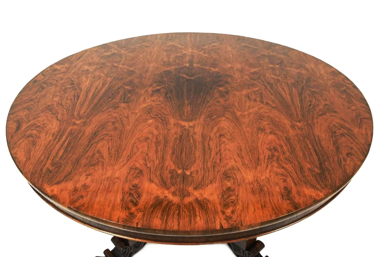 An exceptional round tilt-top table with mellowed rich rosewood of spectacular butterfly veneer. The slab top rests on a narrow crossbanded drum and is supported by an exuberant carved pedestal base with thickly modeled petals and gadrooned base.
