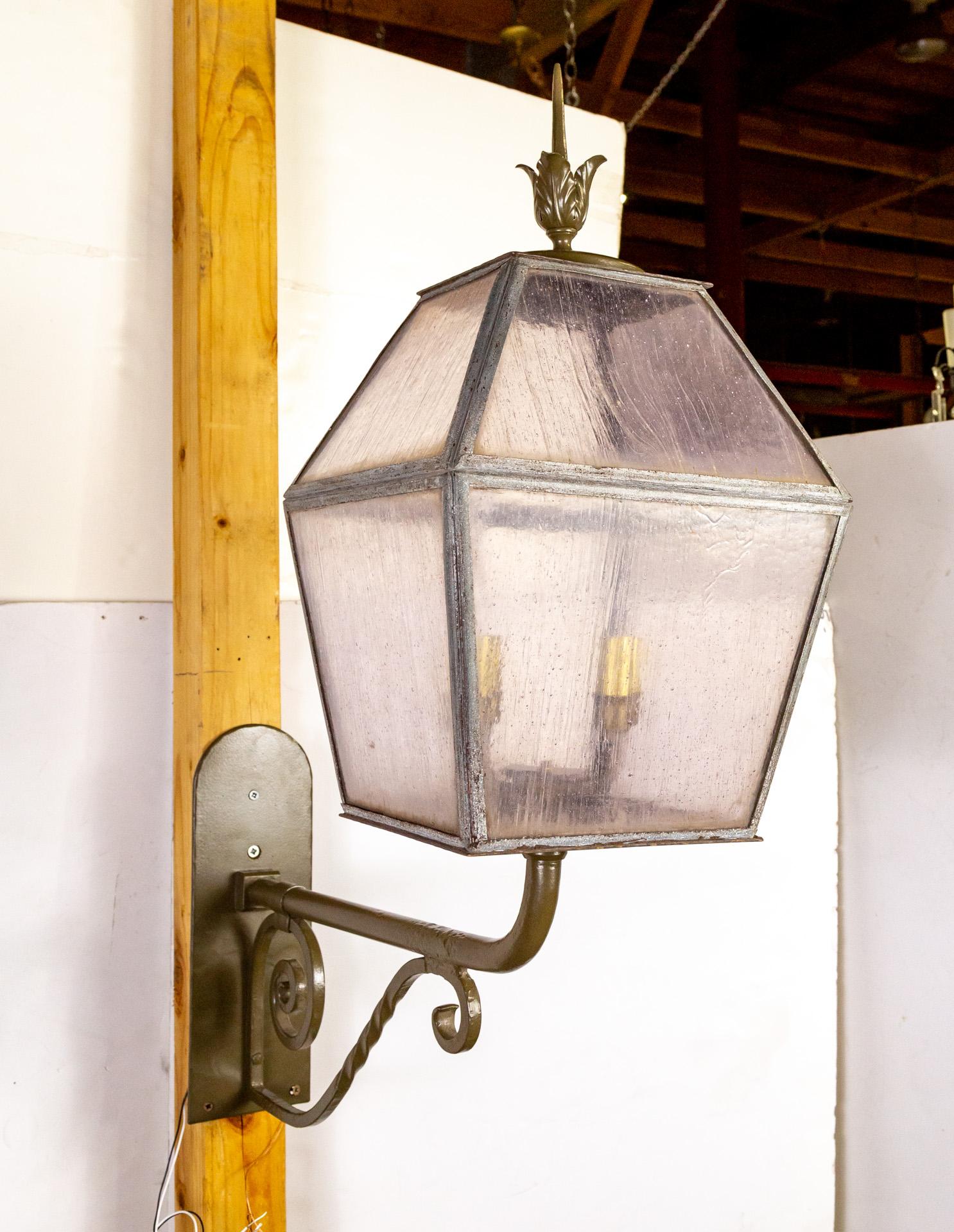 A sizable, 4-light, wall lantern from the early 20th century.  With a freshly powder-coated finial, scroll arm, and backplate.   Newly rewired with brass candle covers. The seeded glass windows are pale lavender.  It has a decorative brass bottom
