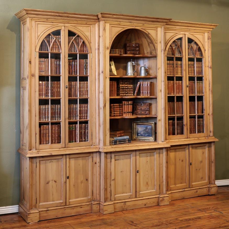 This remarkable, large antique English pine breakfront bookcase is visually stunning. The arched upper glass doors have lovely accent trim adding to the sophistication of this impressive cabinet and complimenting the concave half dome in the center.