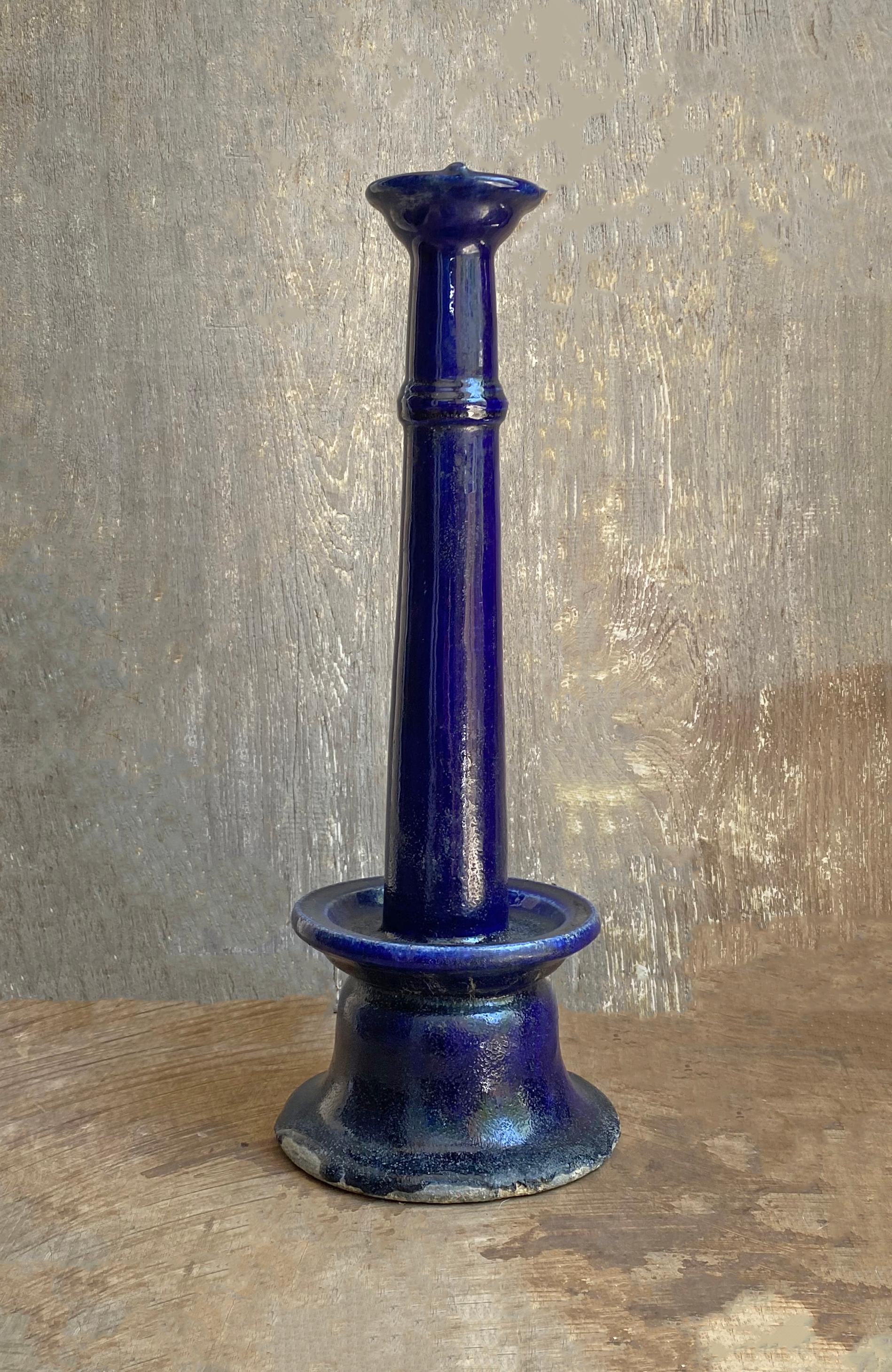 This Chinese oil lamp from the early 20th century features a dark blue glaze which is less common than the more abundant green glaze Chinese oil lamps are often adorned with. This oil lamp is not perfectly straight and bends to one side which has