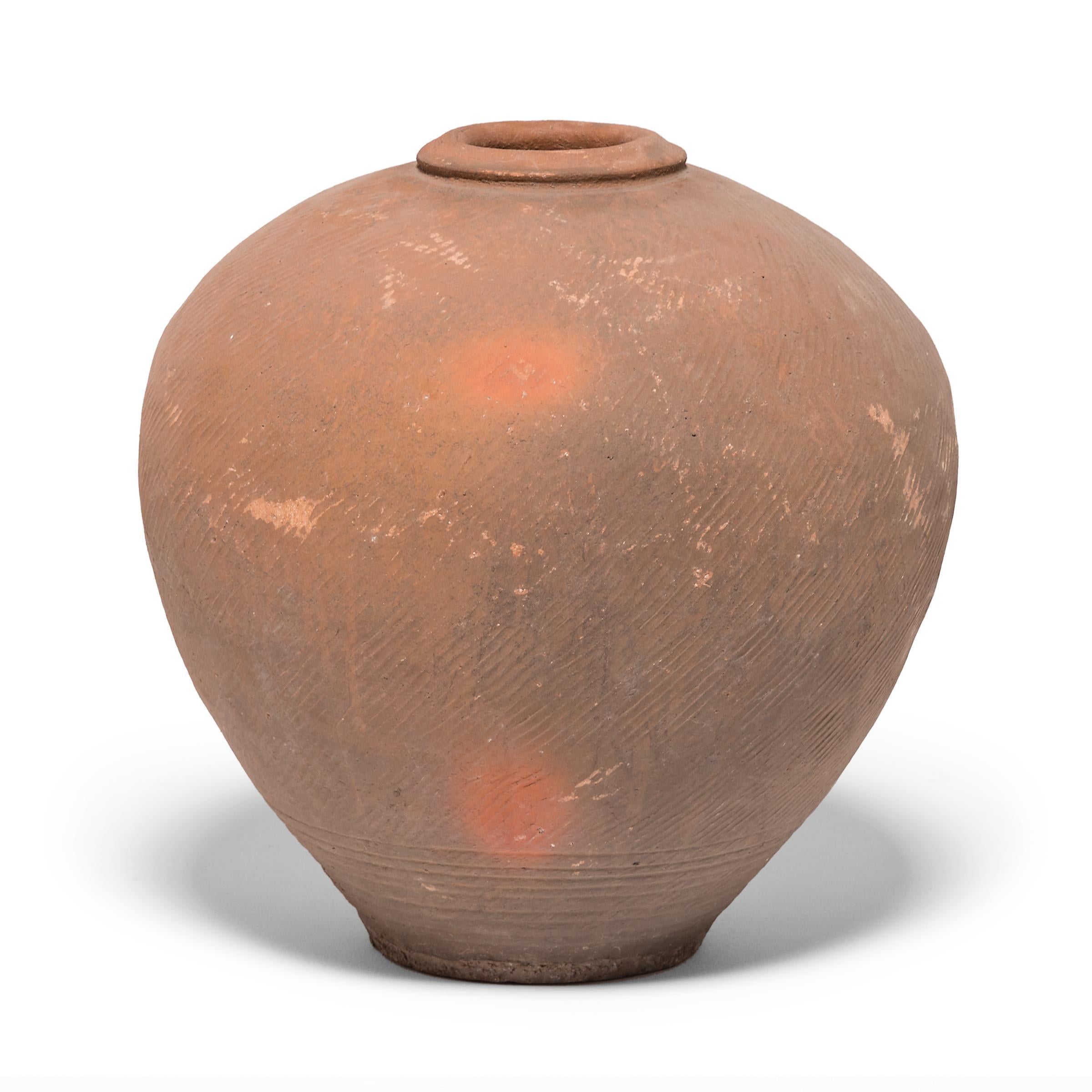 This late 19th century ceramic jar from northern China is formed in a traditional shape meant for storing wine and spirits made from rice and grains. Variation during firing has resulted in delightfully irregular patterns over its textured surface,