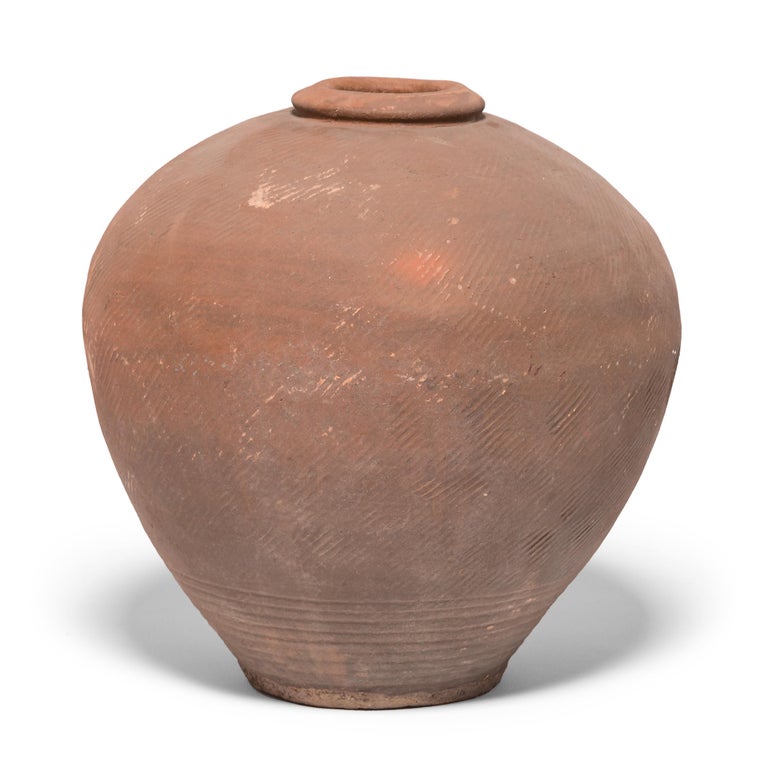 This 19th century ceramic jar from northern China is formed in a traditional shape meant for storing wine and spirits made from rice and grains. Variation during firing has resulted in delightfully irregular patterns over its textured surface, and