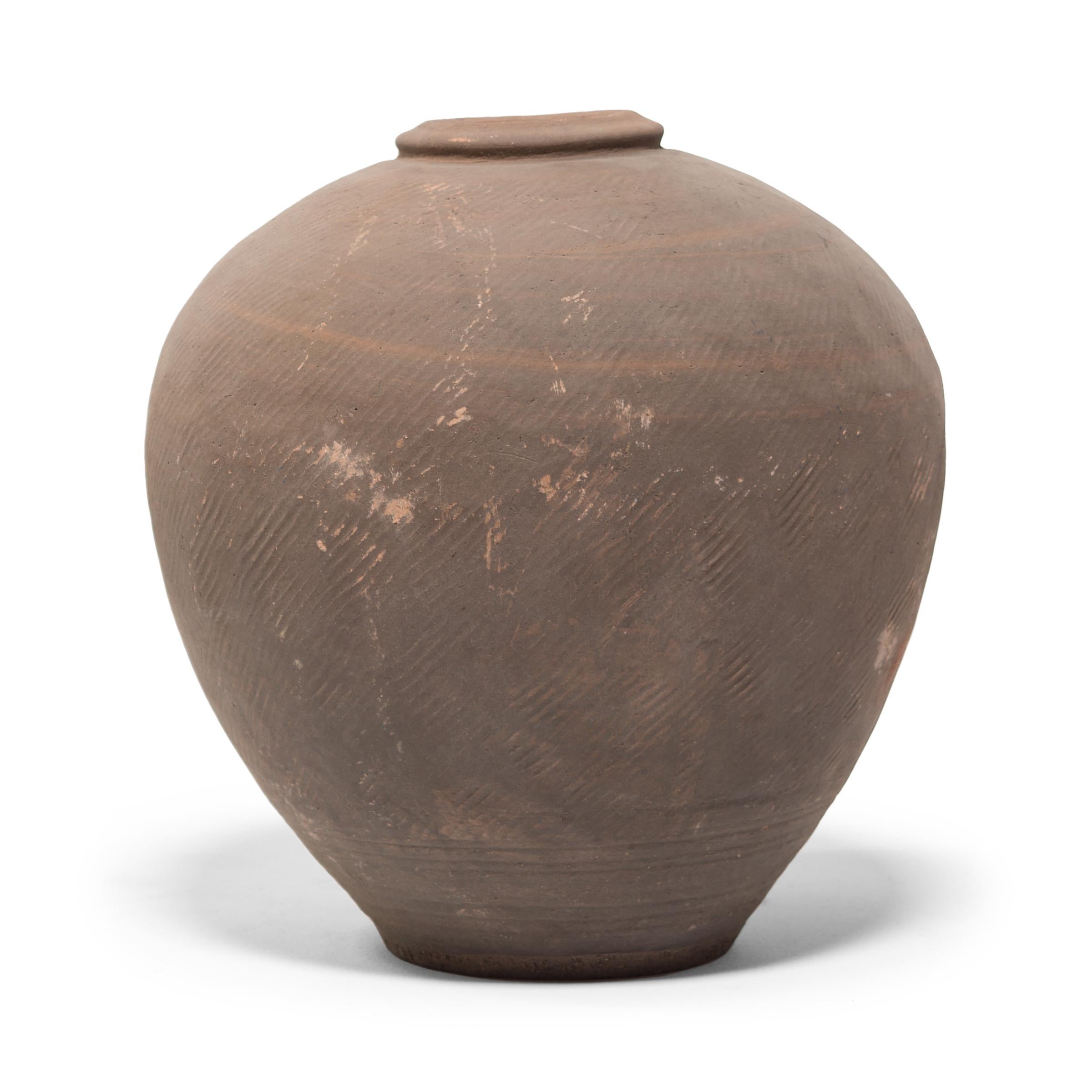 This 19th century ceramic jar from northern China is formed in a traditional shape meant for storing wine and spirits made from rice and grains. Variation during firing has resulted in delightfully irregular patterns over its textured surface, and