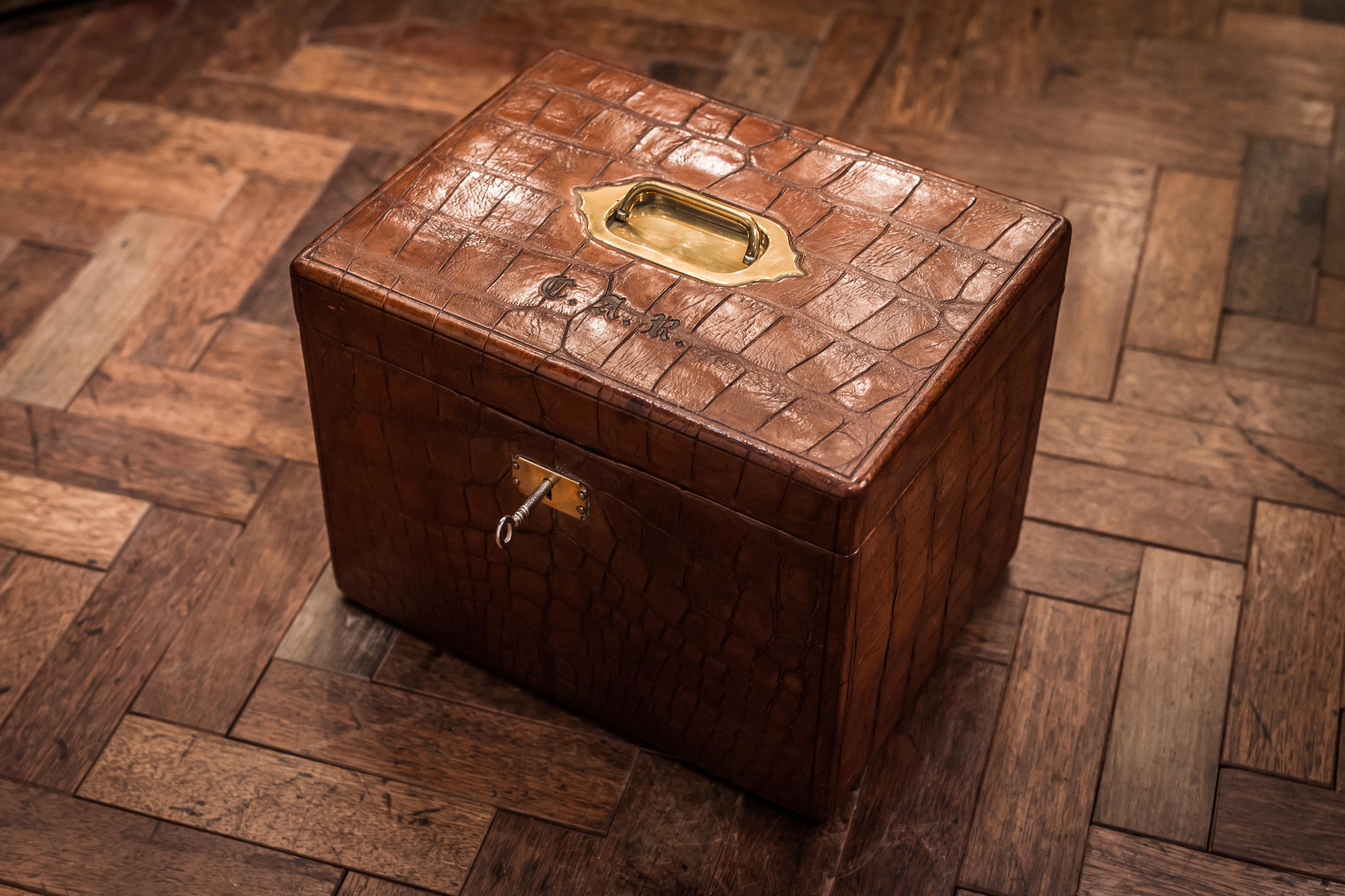 A large early 20th century crocodile Jewellery Box of rectangular form, the hinged lid centred by flush, brass-sunk carrying handle, initialled 'C.A.R.', opening to reveal an aubergine-coloured silk and leather interior with three compartmented
