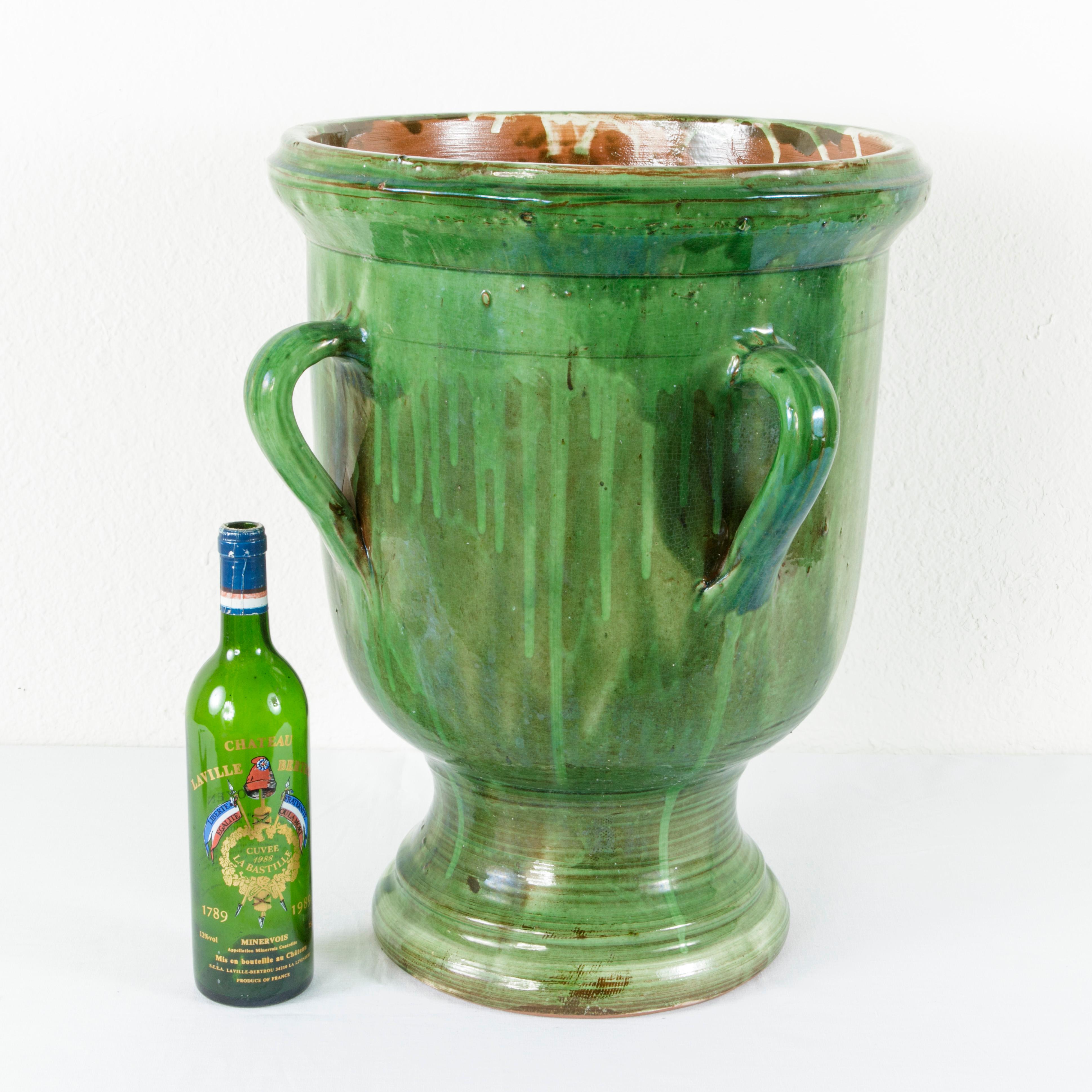 From the region of Provence in Southern France, this early 20th century faience urn stands at an impressive 20.75 inches in height. The urn is glazed in a Classic green and features four handles. A beautiful planter or cachepot, circa 1910.