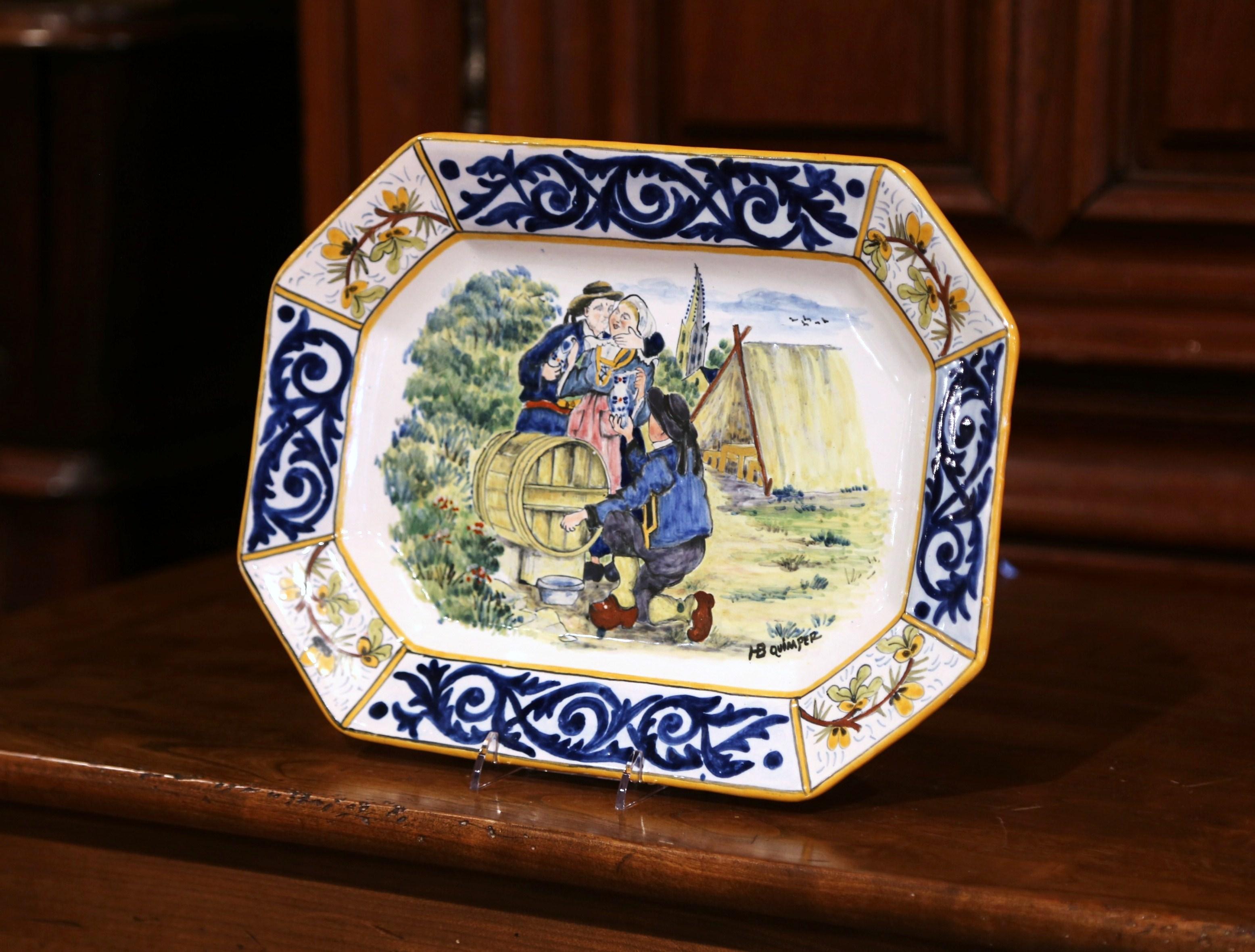 Decorate a wall of a shelf with this colorful antique platter; created in Brittany, France circa 1920, the hand painted ceramic plate features a happy drinking scene with wine maker handing pitcher to a woman while she being kissed by a man. The
