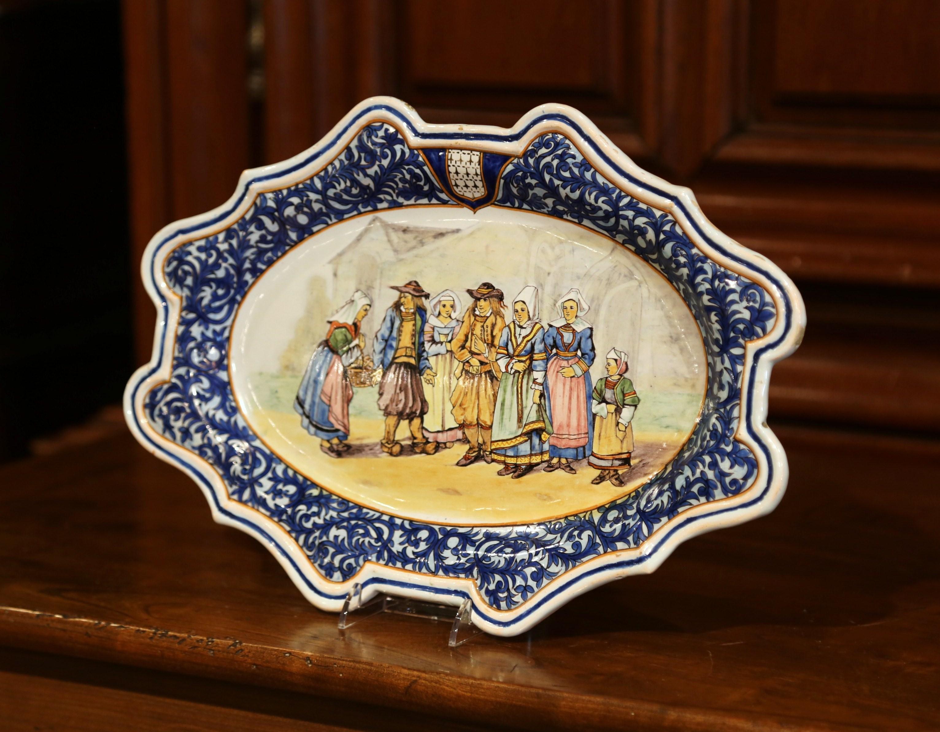 Decorate your kitchen or breakfast room with this elegant ceramic wall charger; crafted in Quimper circa 1905, the faience oval plate with blue border and a centre coat of arms of Brittany, features seven Britons people in traditional clothing