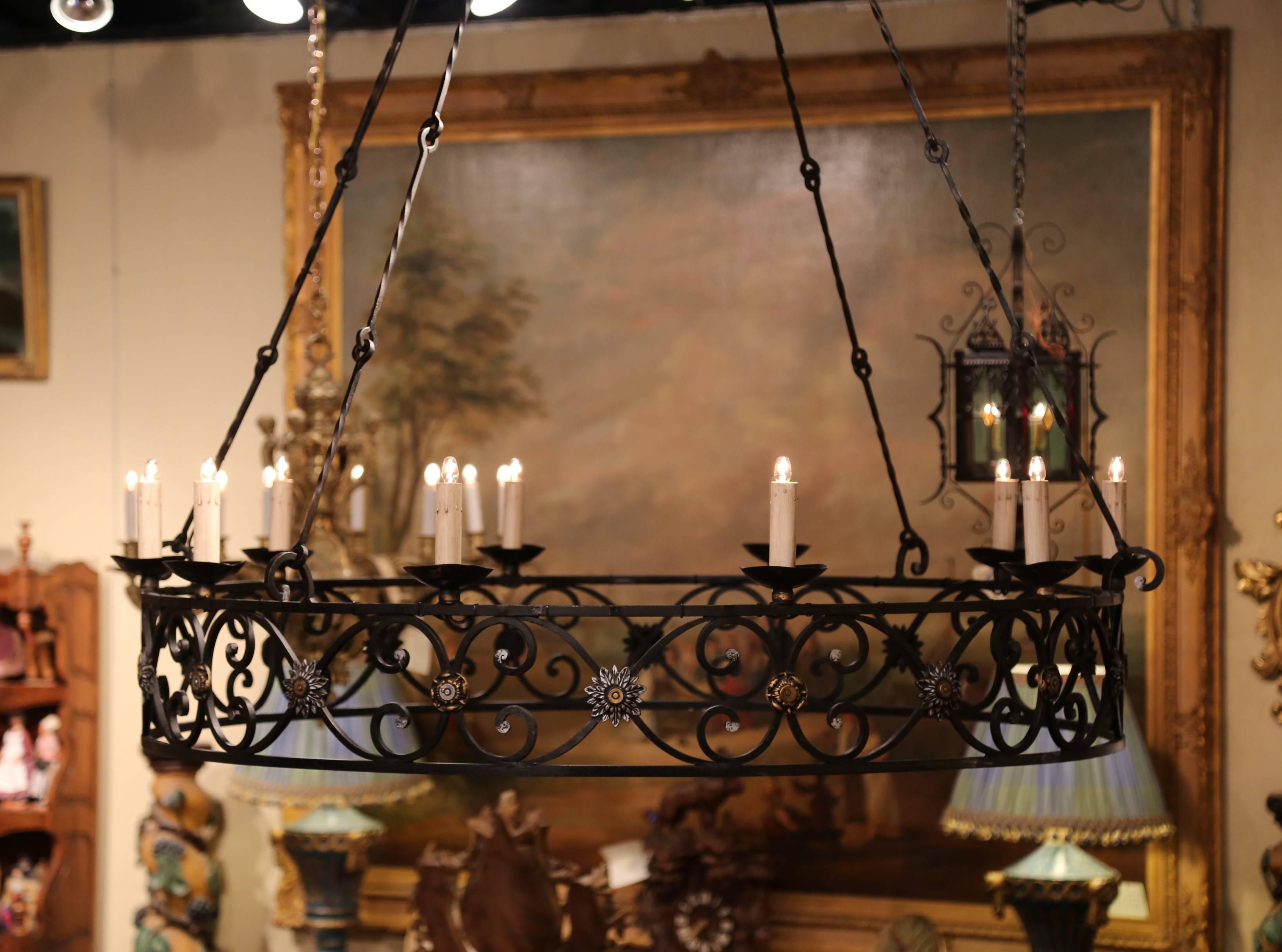 This monumental antique light fixture was created in Normandy, France; crafted circa 1920, the Gothic style chandelier features ten lights newly wired over a large iron gallery with scrolls and flowers medallions. It has the original four chains