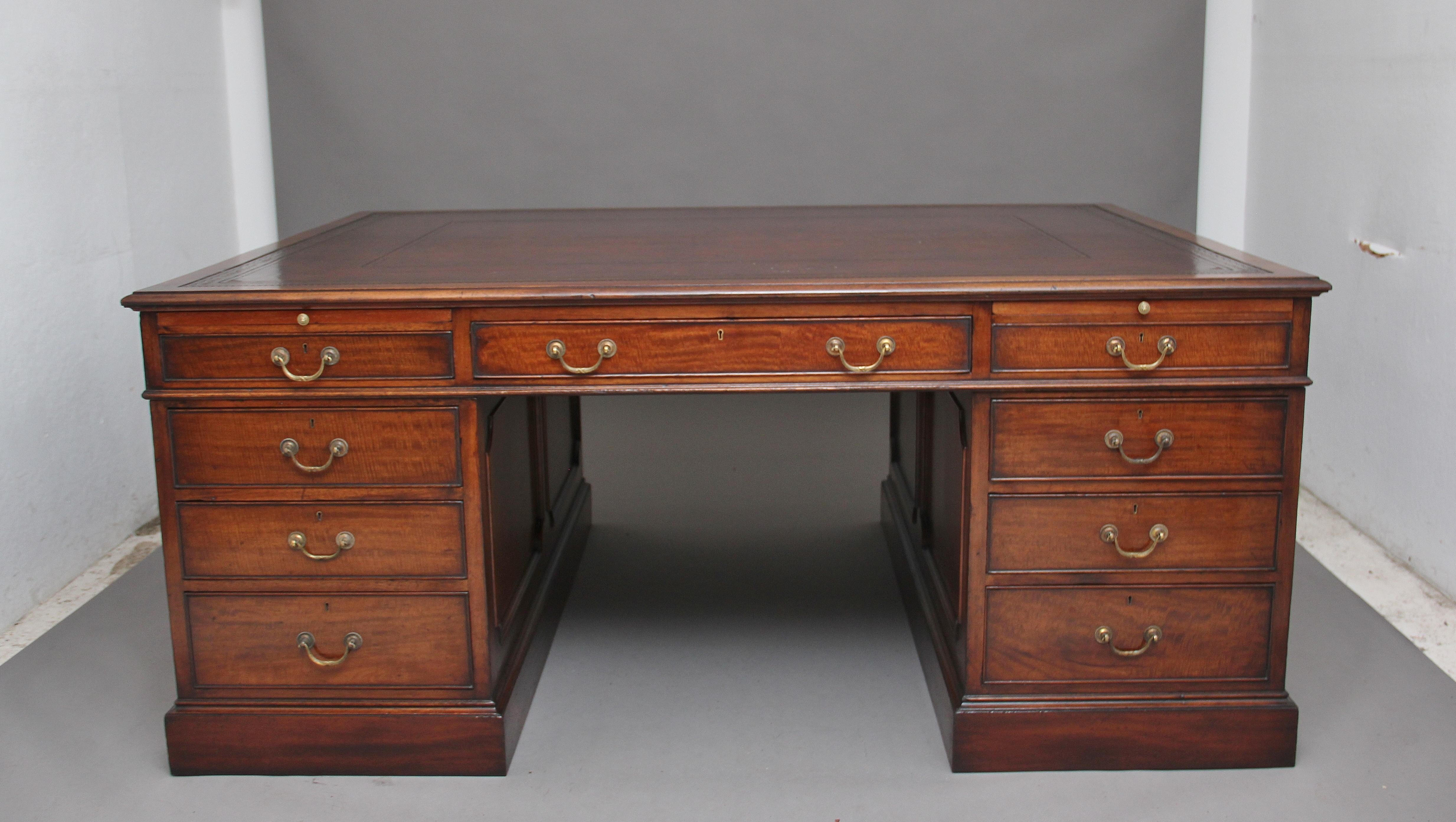 A large early 20th century mahogany twin pedestal partners desk by “White Allom & Company of London”, the moulded edge top having a brown leather writing surface decorated with gold and blind tooling, the front of the desk having an arrangement of
