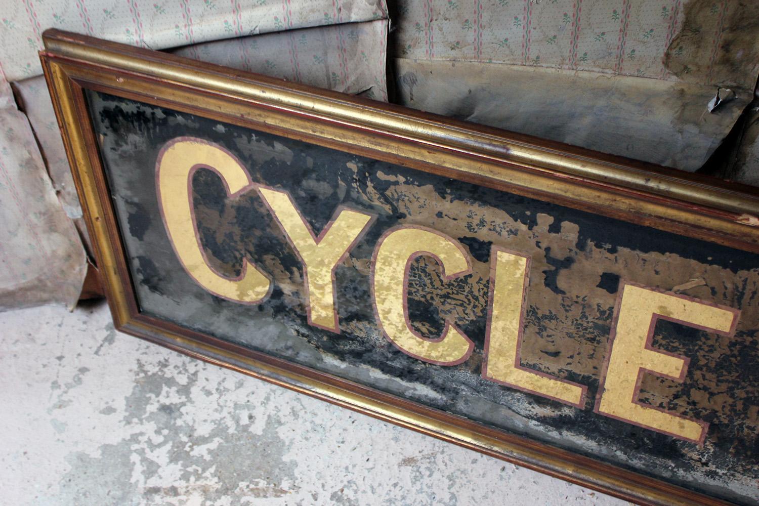 The wonderfully decorative and imposing reverse glass painted advertising sign for a Cycle Maker, at six and a half feet long, the mirrored gold lettering with pink edgings to an inky blue black ground, the whole in a good quality period gilt frame