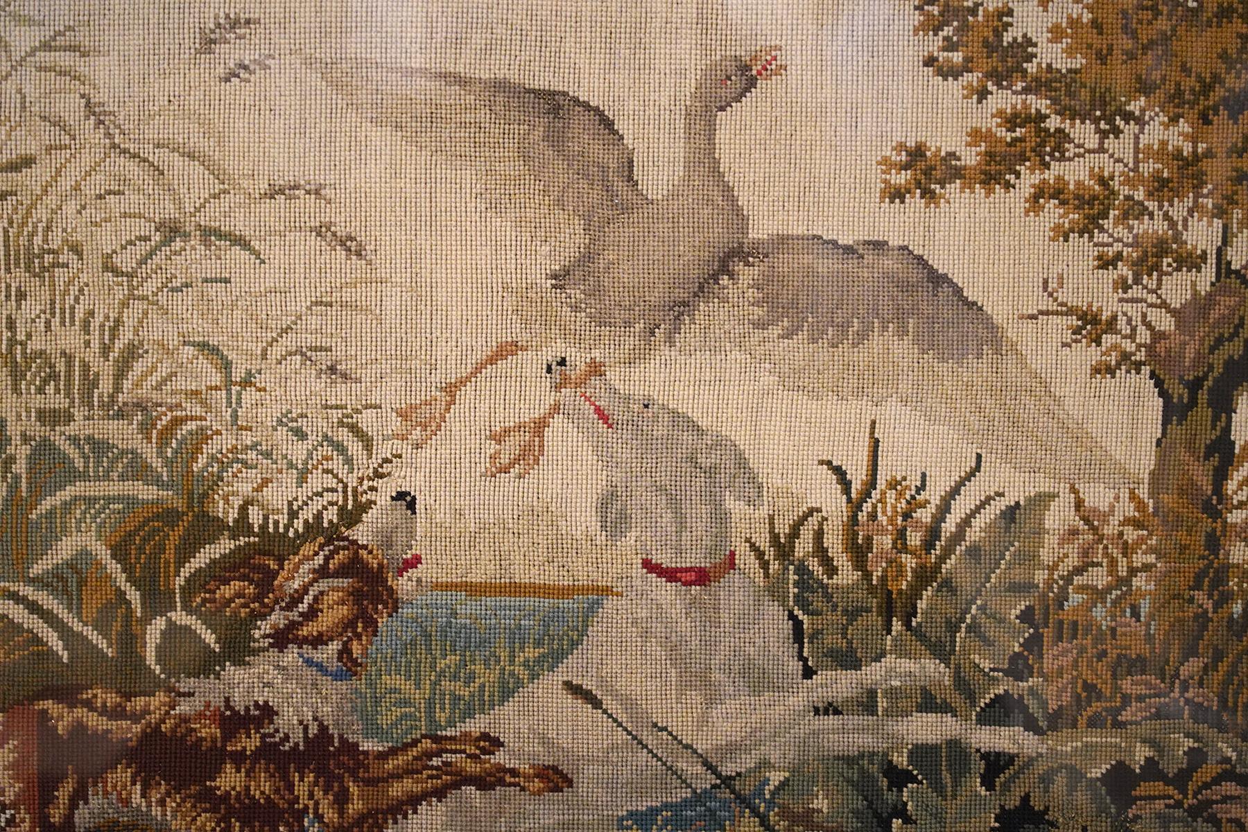 This rare English needlepoint is signed with initials and year 1840 in the lower left corner. It depicts two dogs and a flying duck in a lake landscape and the entire needlepoint is shaped and bordered with leafwork and foliate scrolls. The
