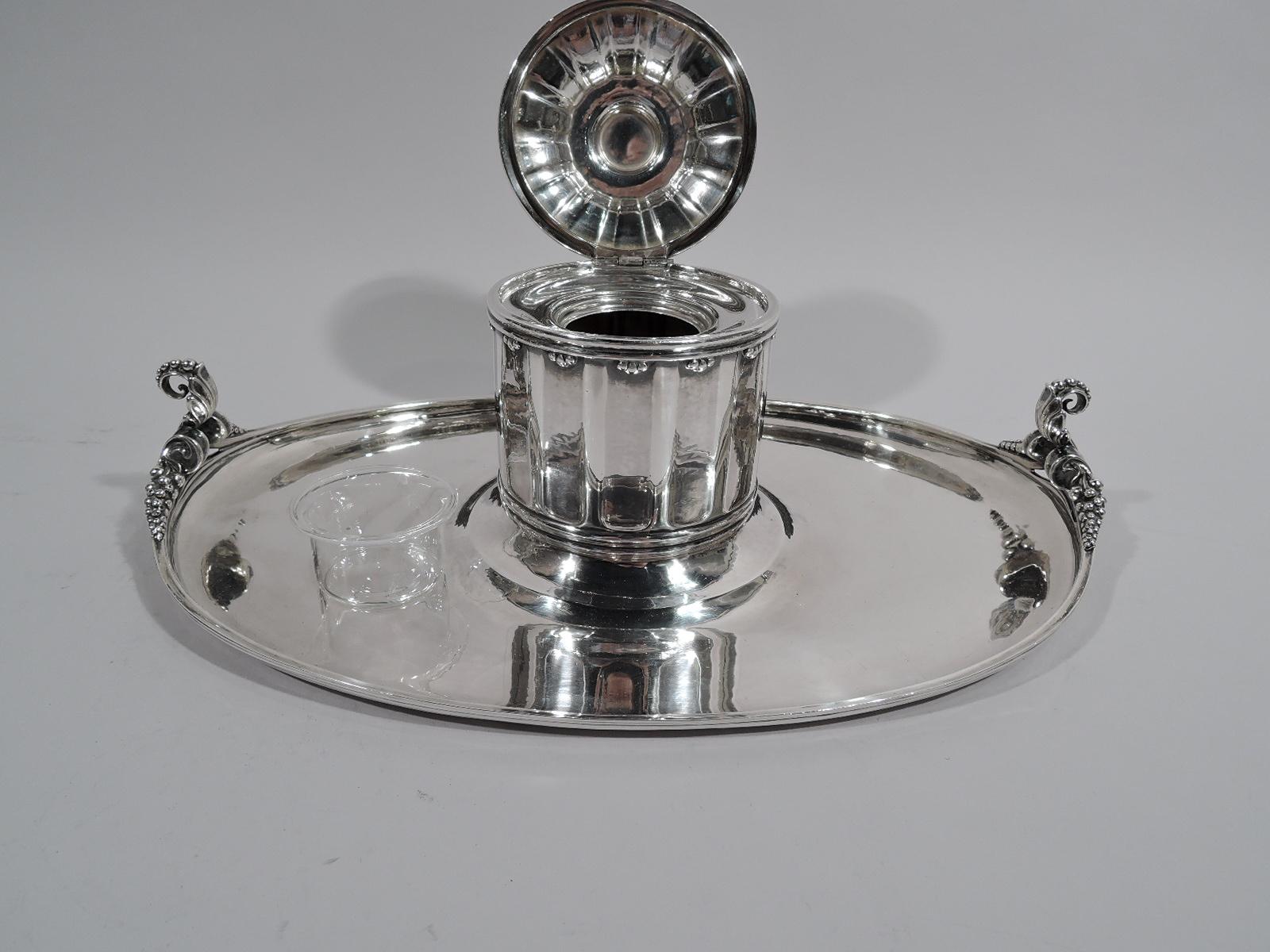 Rare Art Nouveau sterling silver inkstand. Made by Georg Jensen in Copenhagen. Fluted columnar drum with raised and hinged cover. Cover top has large bud finial with 4 beaded and scrolled mounts set in pebble-beaded border. Mounted to oval tray with