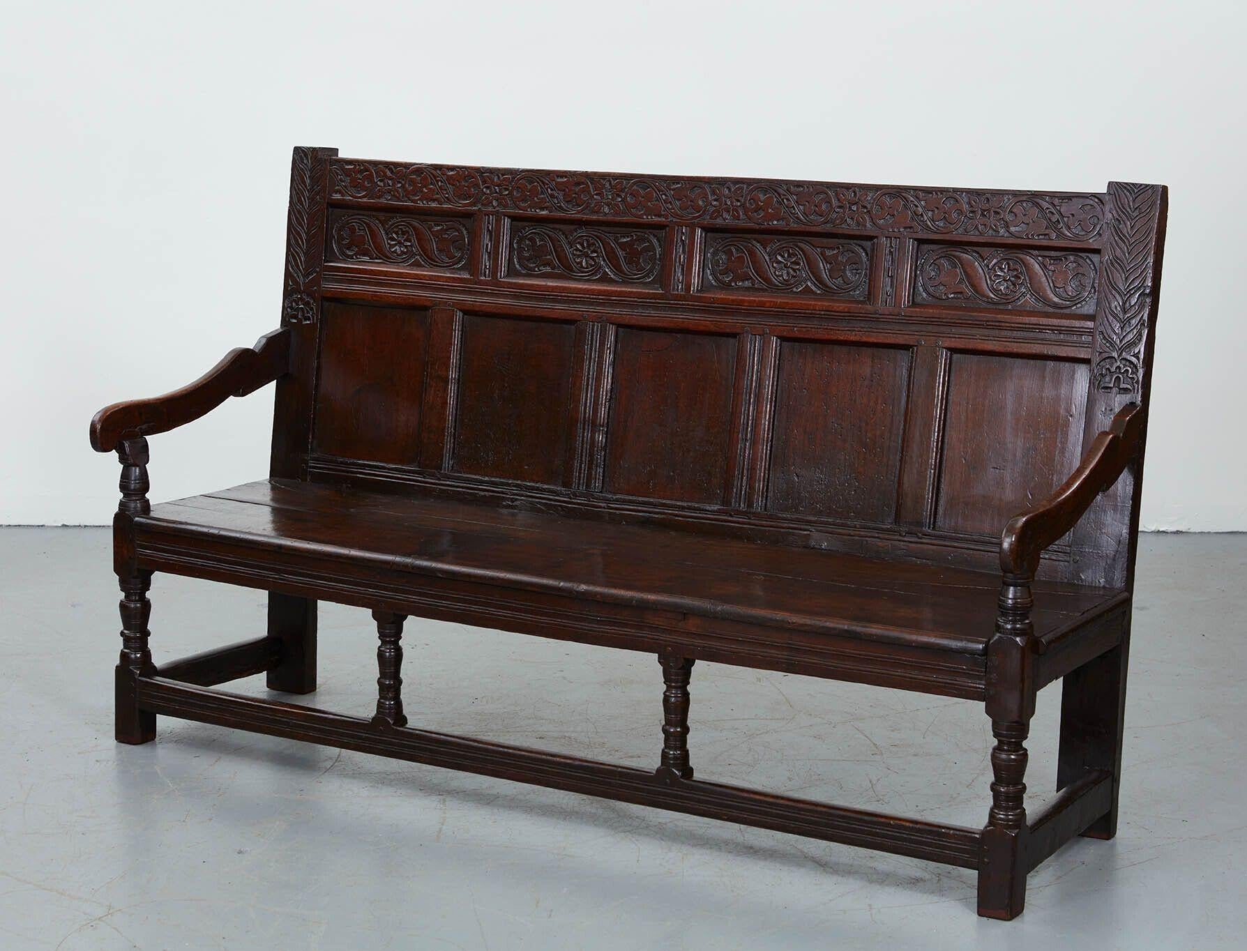 A large early English bog oak paneled back settle, circa 1680.  Of generous proportions, with a series of railed panels on back and carved elements above, shaped downward sloping arms and boarded seat with carved apron supported on front and side