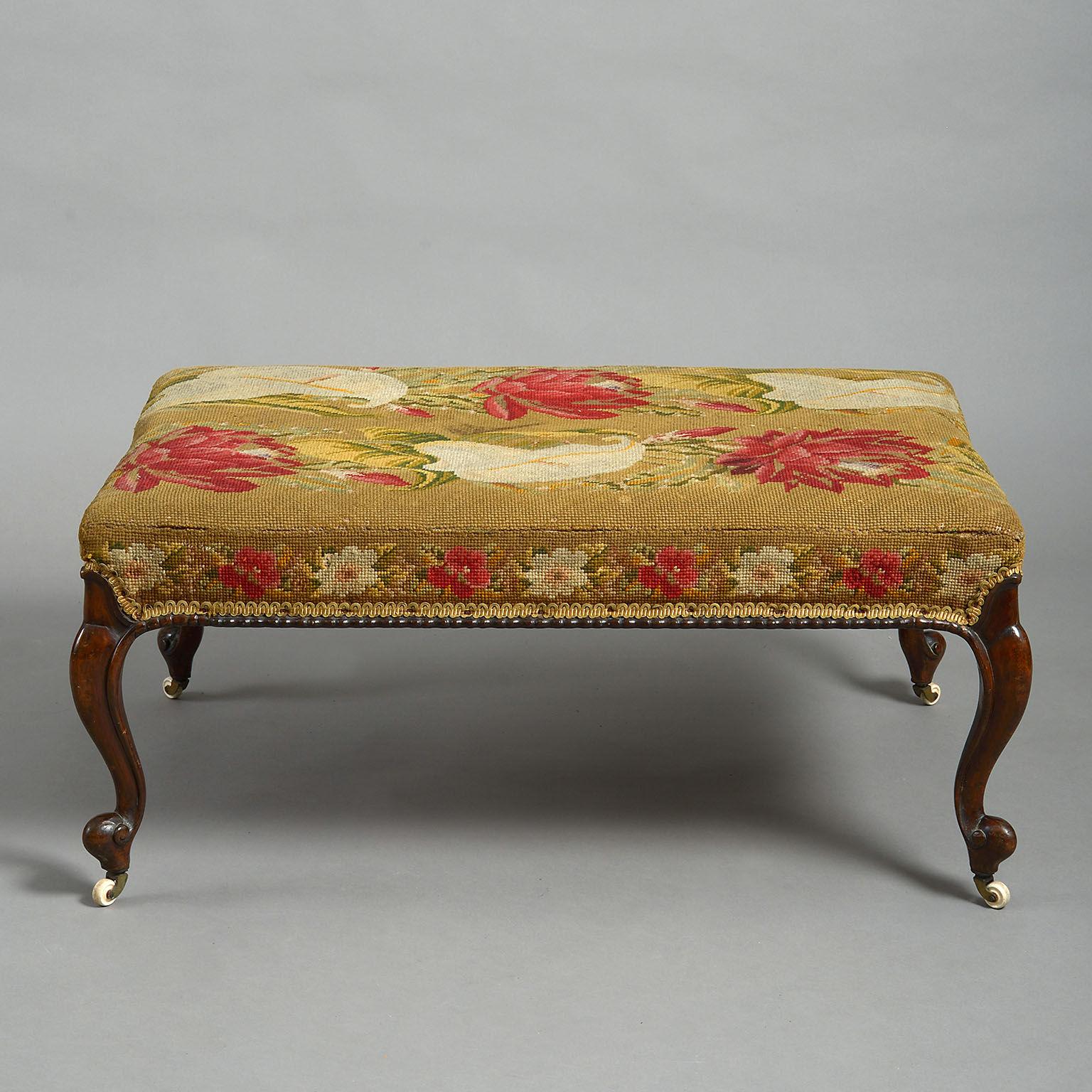 Large early Victorian walnut stool, the rectangular upholstered top covered in original needlework, raised on moulded cabriole legs terminating in white porcelain castors. Perfect to double as a coffee table.