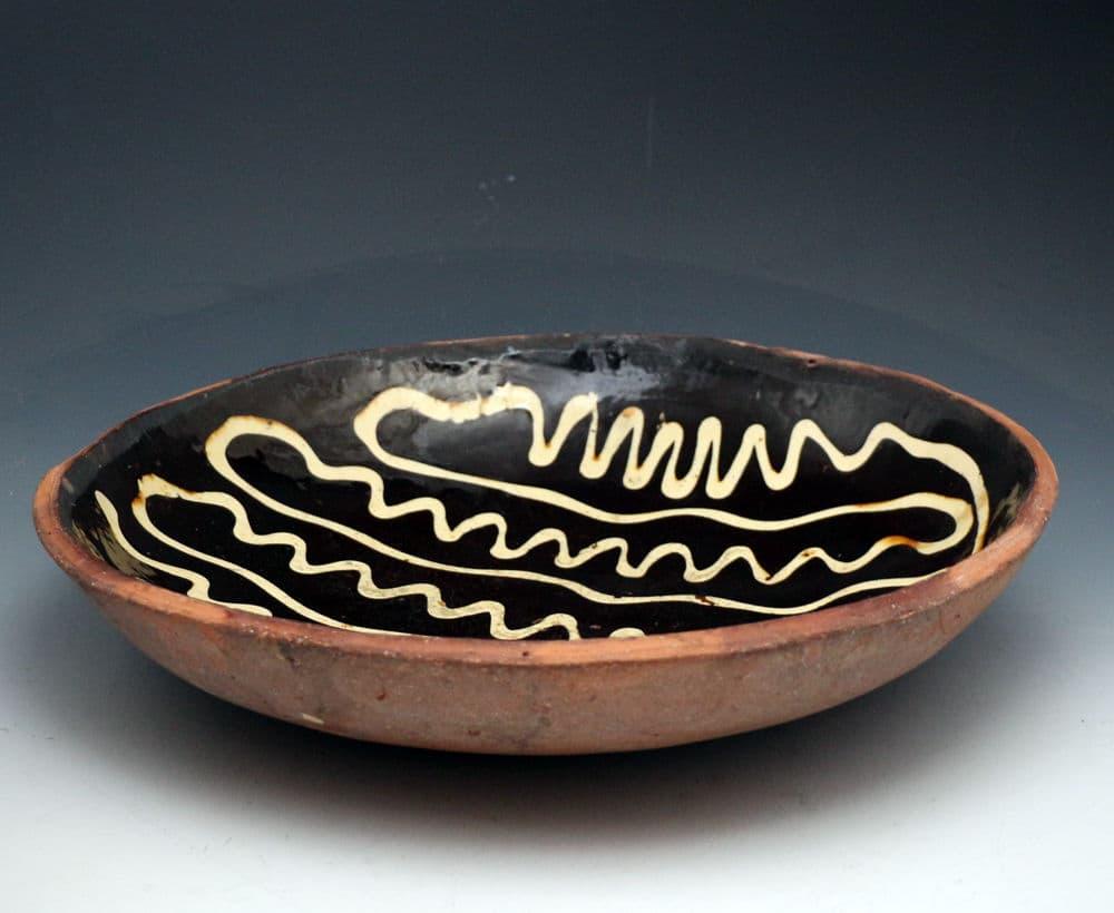 A large striking earthenware slipware loaf baking dish on a dark chocolate brown ground with a creamy trailing slip decoration executed boldly and competently. The dish has an additional significant presence of exceptional size at 16.5 inches