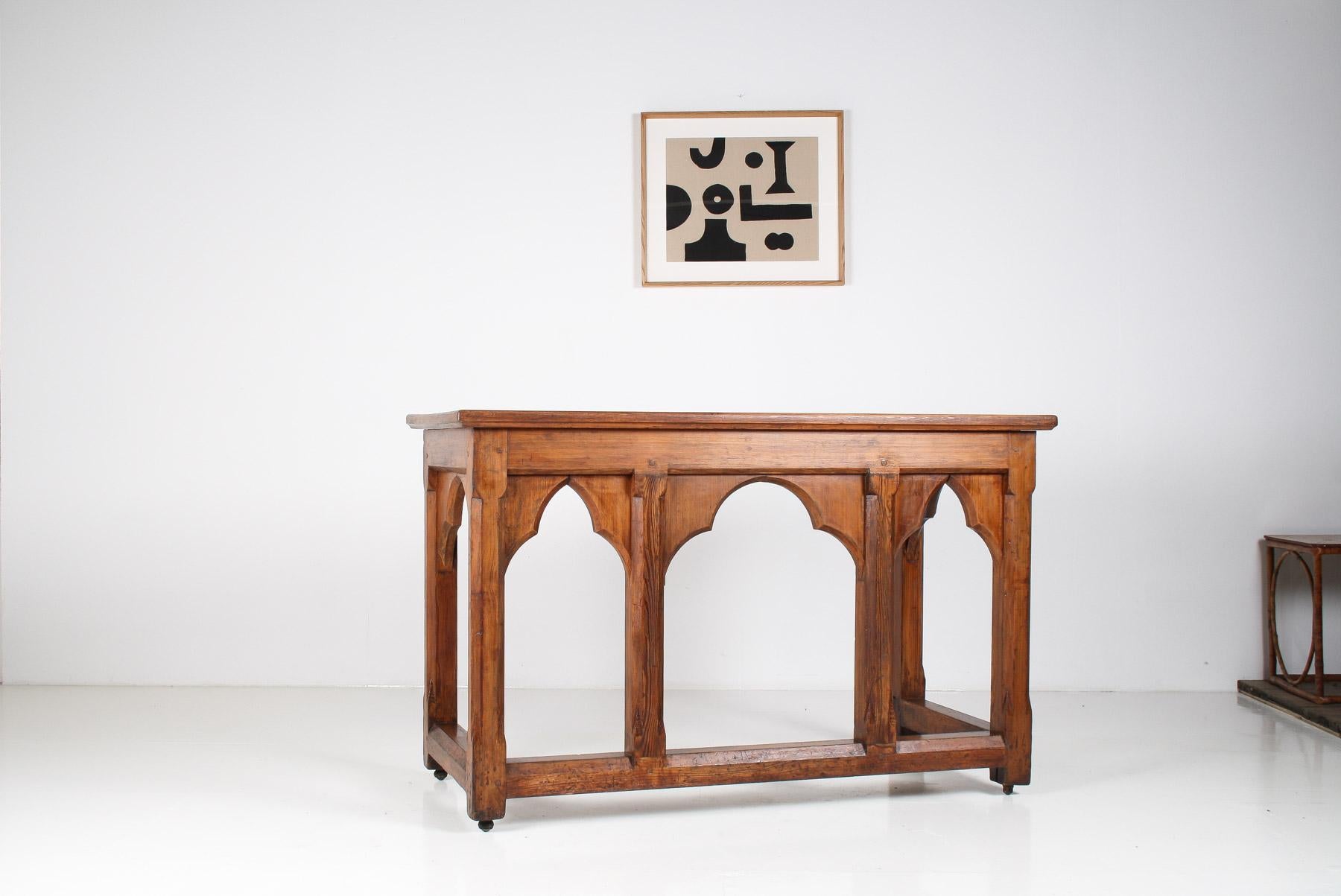 This large, circa 1860, Victorian Ecclesiastical Gothic Revival altar table is crafted from solid pitch pine and features a two-planked top supported by a robust peg and mortised base. The design includes inset trefoil arched panels and heavy square