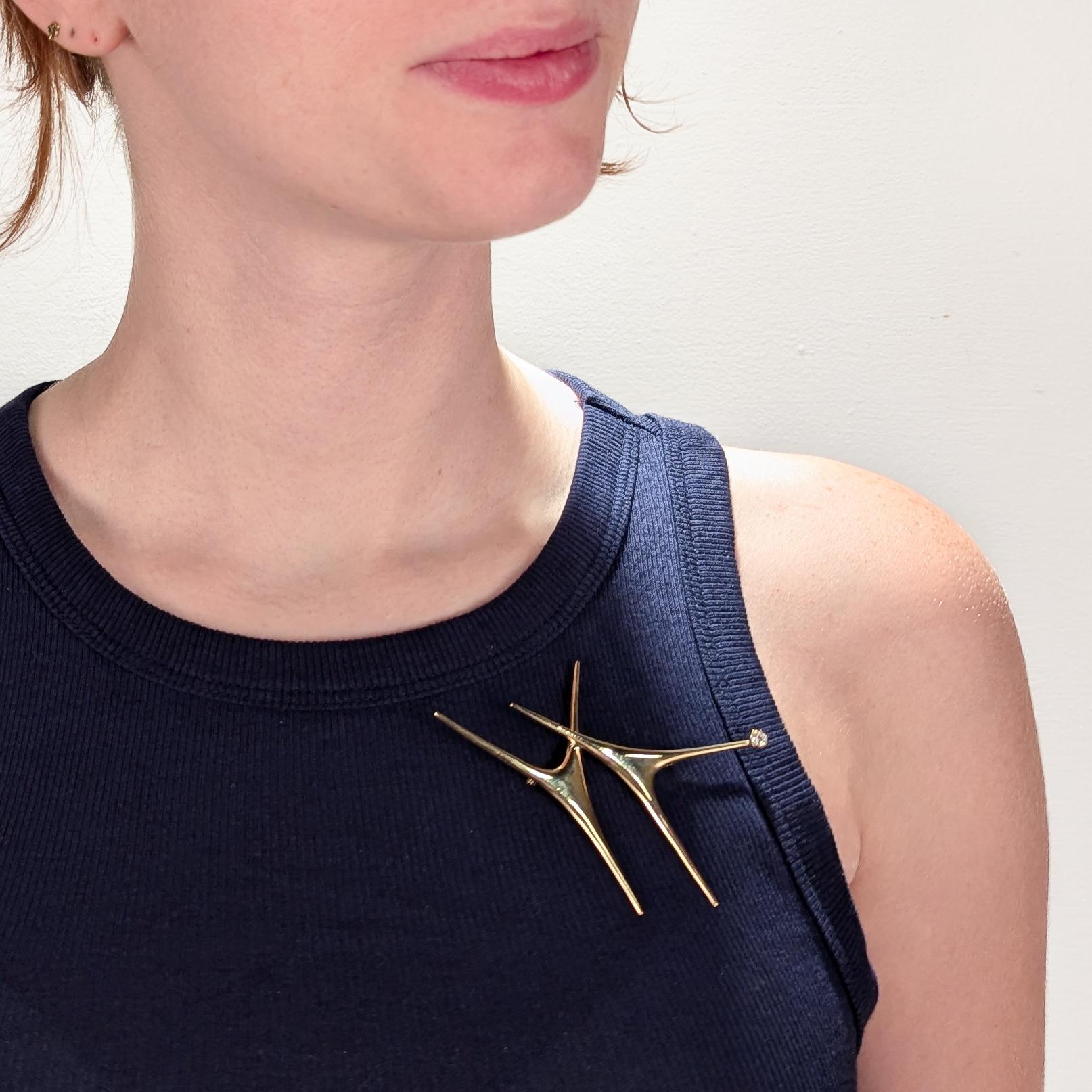 A fine Modernist brooch.

By Ed Wiener, the renowned New York City Mid-Century jewelry maker.

Comprising 2 conjoined abstract 3-prong elements. One set with a round cut diamond to its end. Secured with a pin and catch to its reverse.

Ed Wiener was